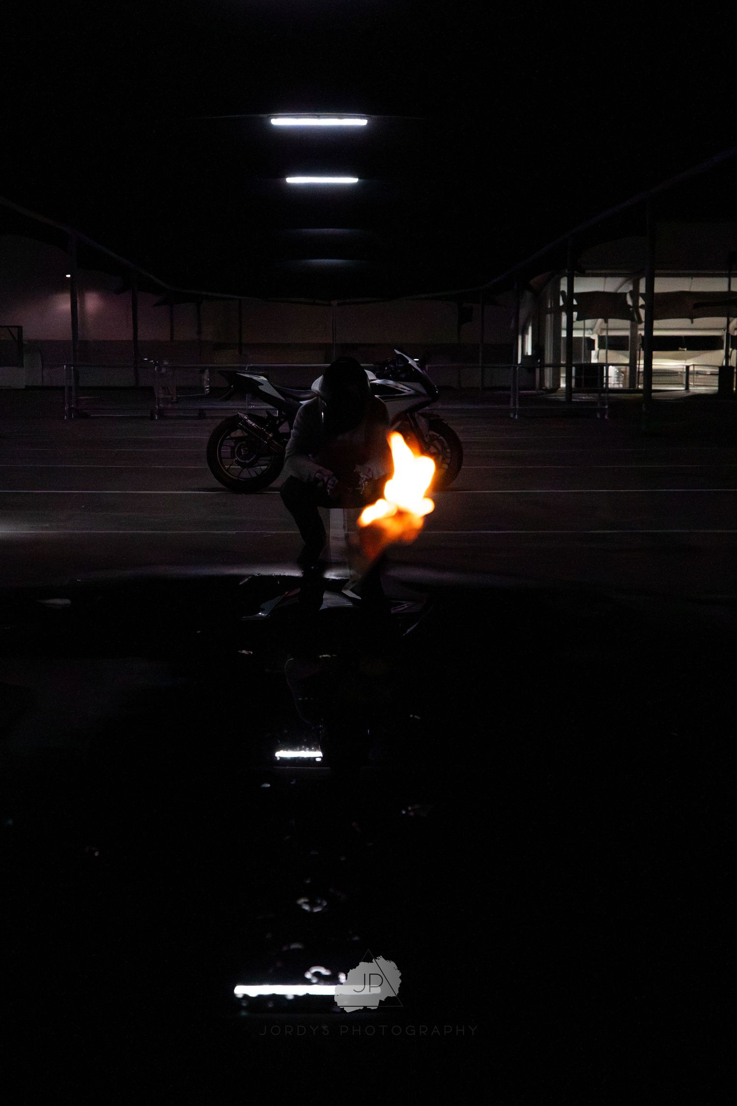 A motorcycle stunt sequence captured at night showing flames and silhouettes in a parking structure.