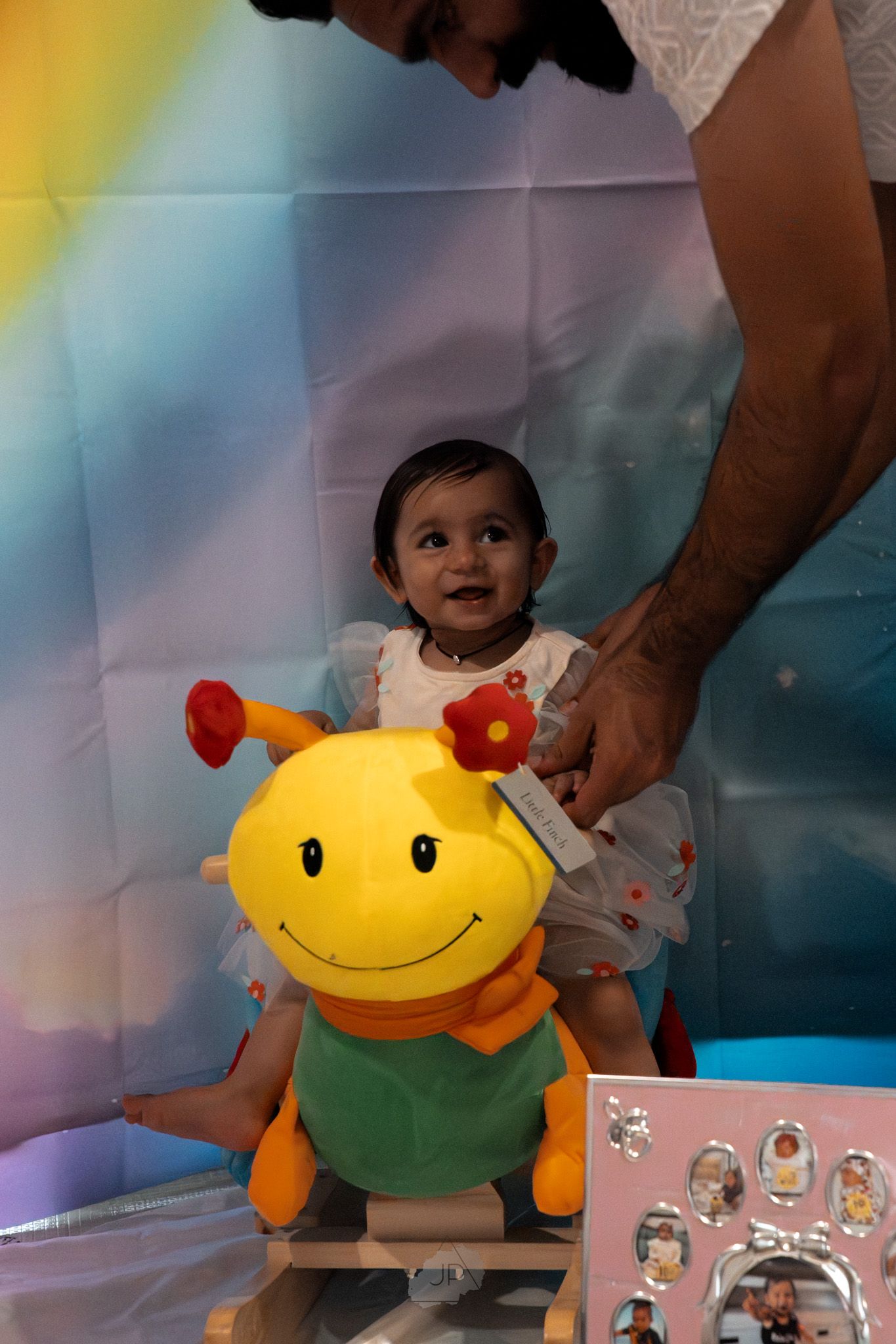 A child sits with a large plush yellow and orange bee toy against a colorful background during a photo session.