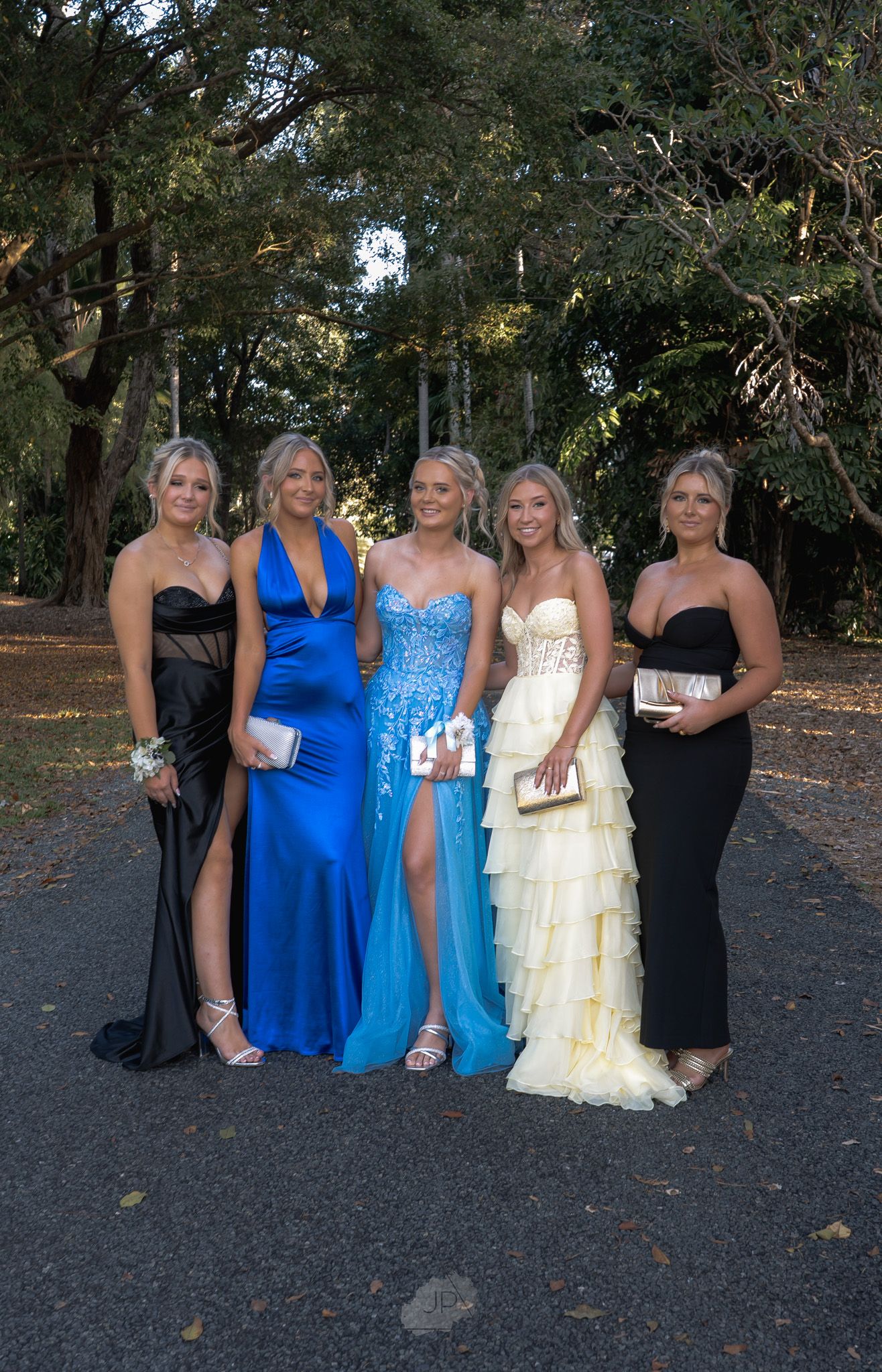 A group in formal attire poses outdoors, wearing black and blue dresses against a wooded background.