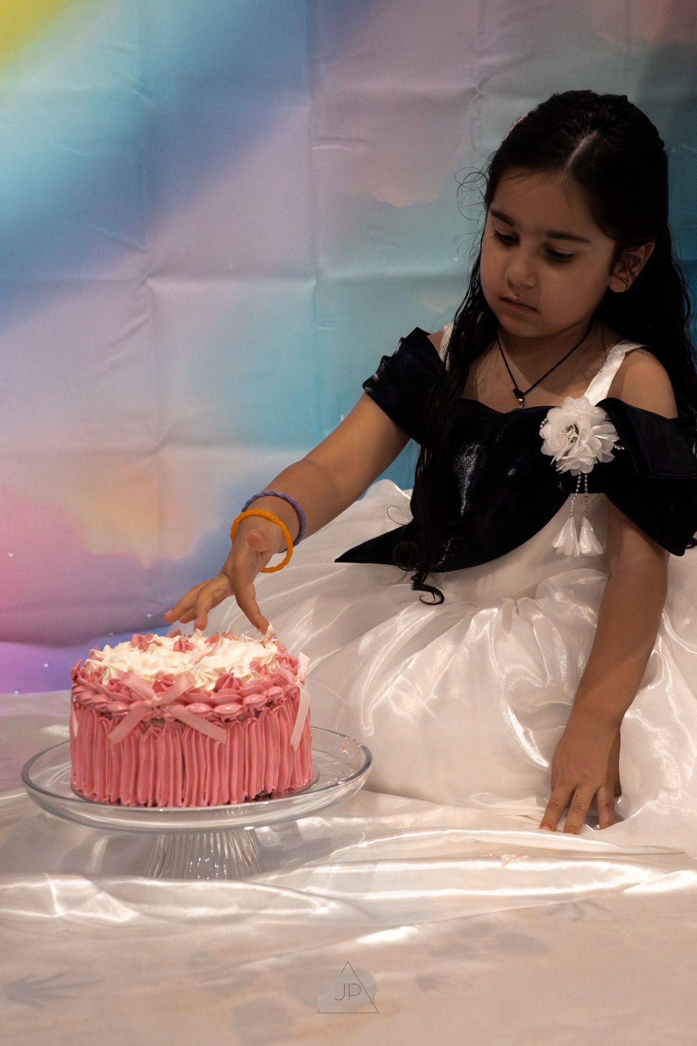 A series of photos showing someone in a white dress decorating a pink frosted cake on a white tablecloth.