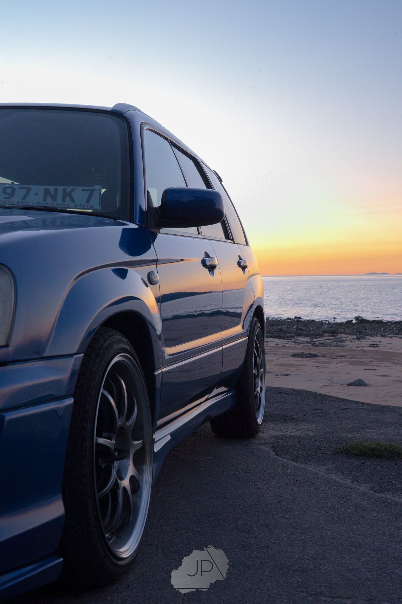 Sleek silver BMW M3 photographed at sunset against a coastal horizon with custom black wheels and lowered suspension.