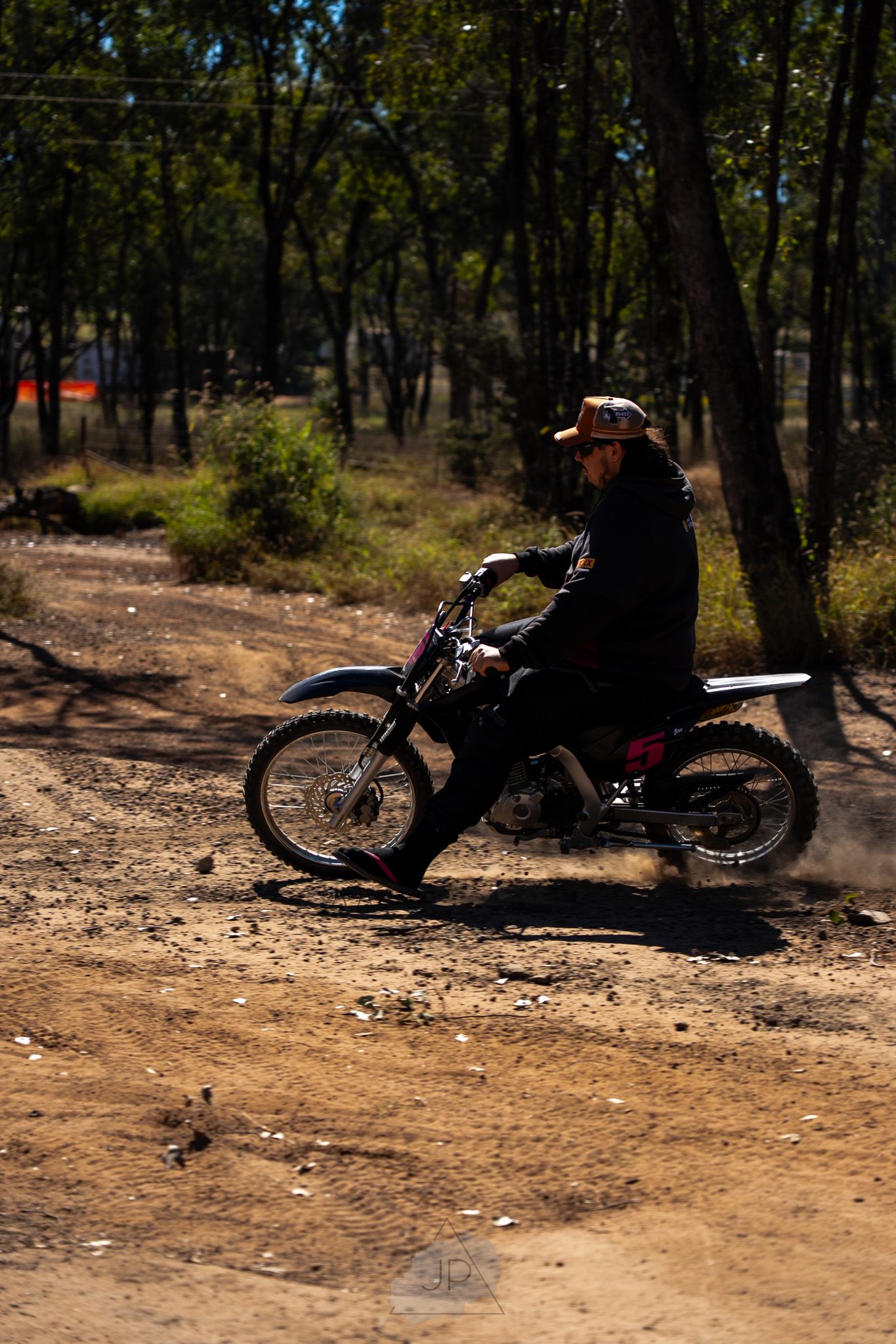 Black dirt bike shown from various angles parked on a dusty forest trail surrounded by trees and natural lighting.