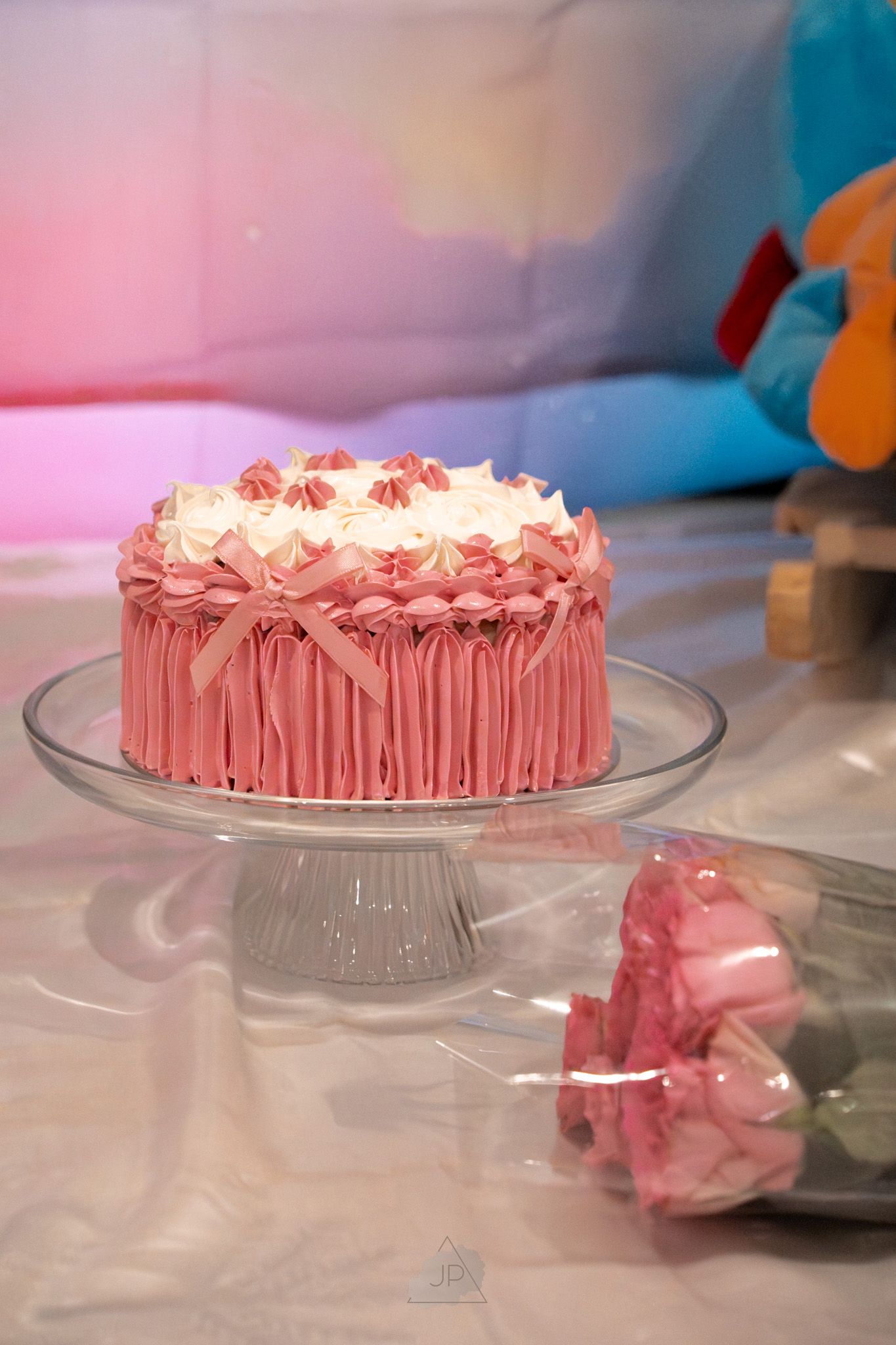 A pink frosted cake with decorative piping sits on a glass cake stand in a series of similar shots.
