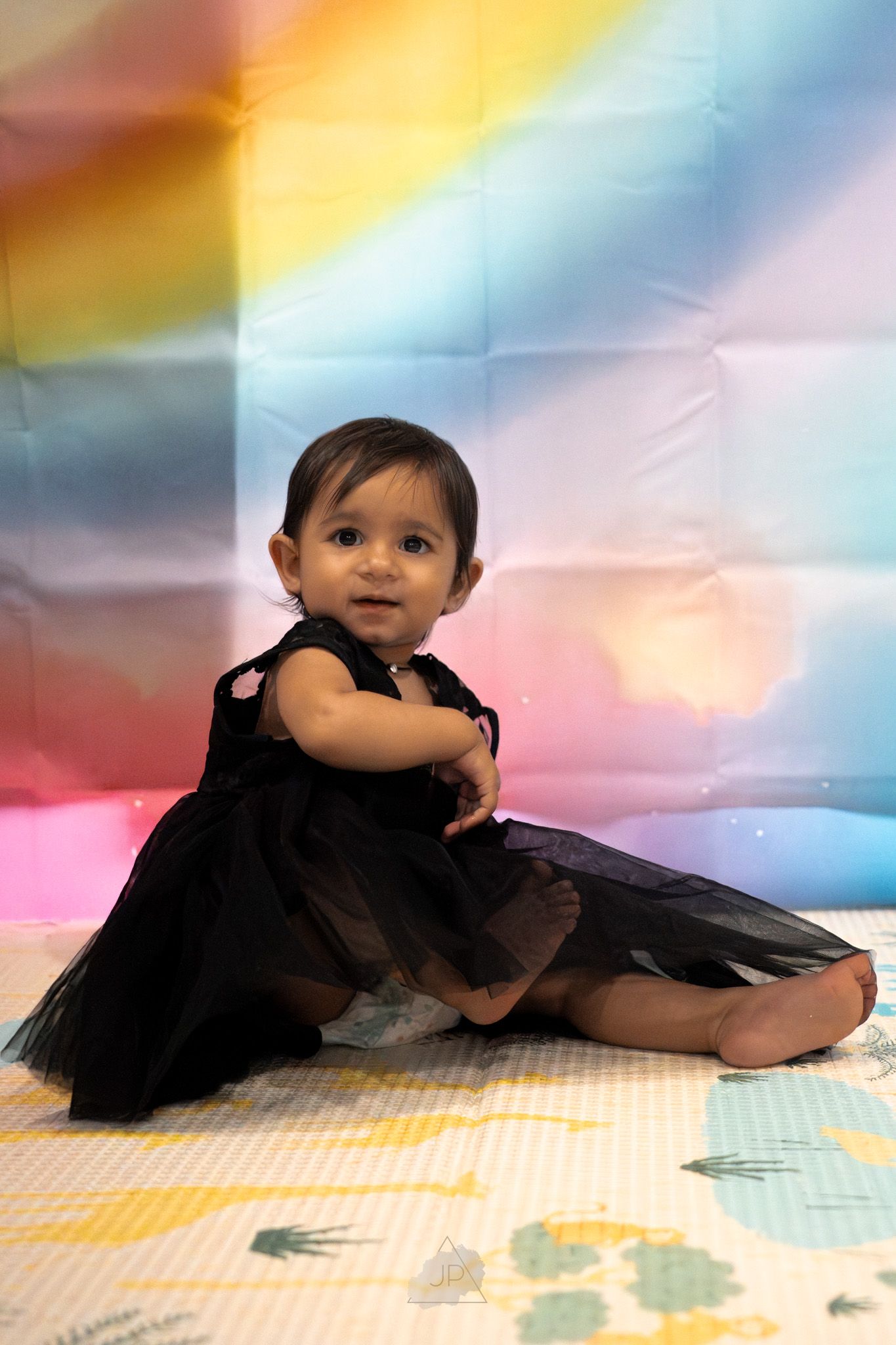 A baby in a black tutu dress poses on a colorful backdrop in a series of connected photos.