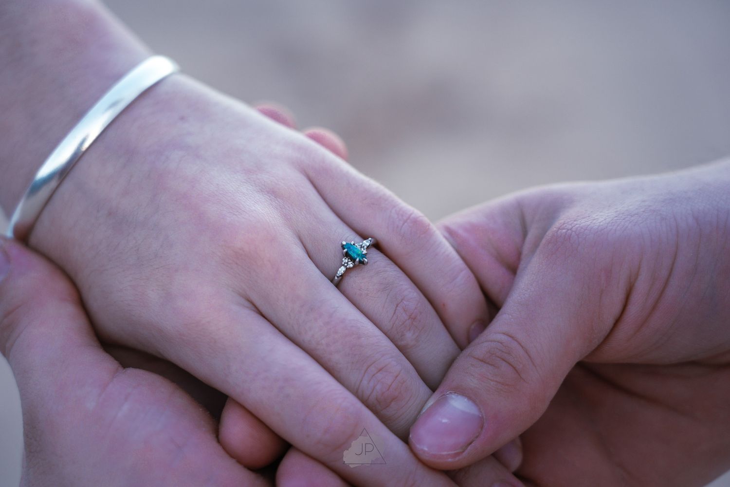 Two hands exchange wedding rings during an intimate ceremony against a blurred background.