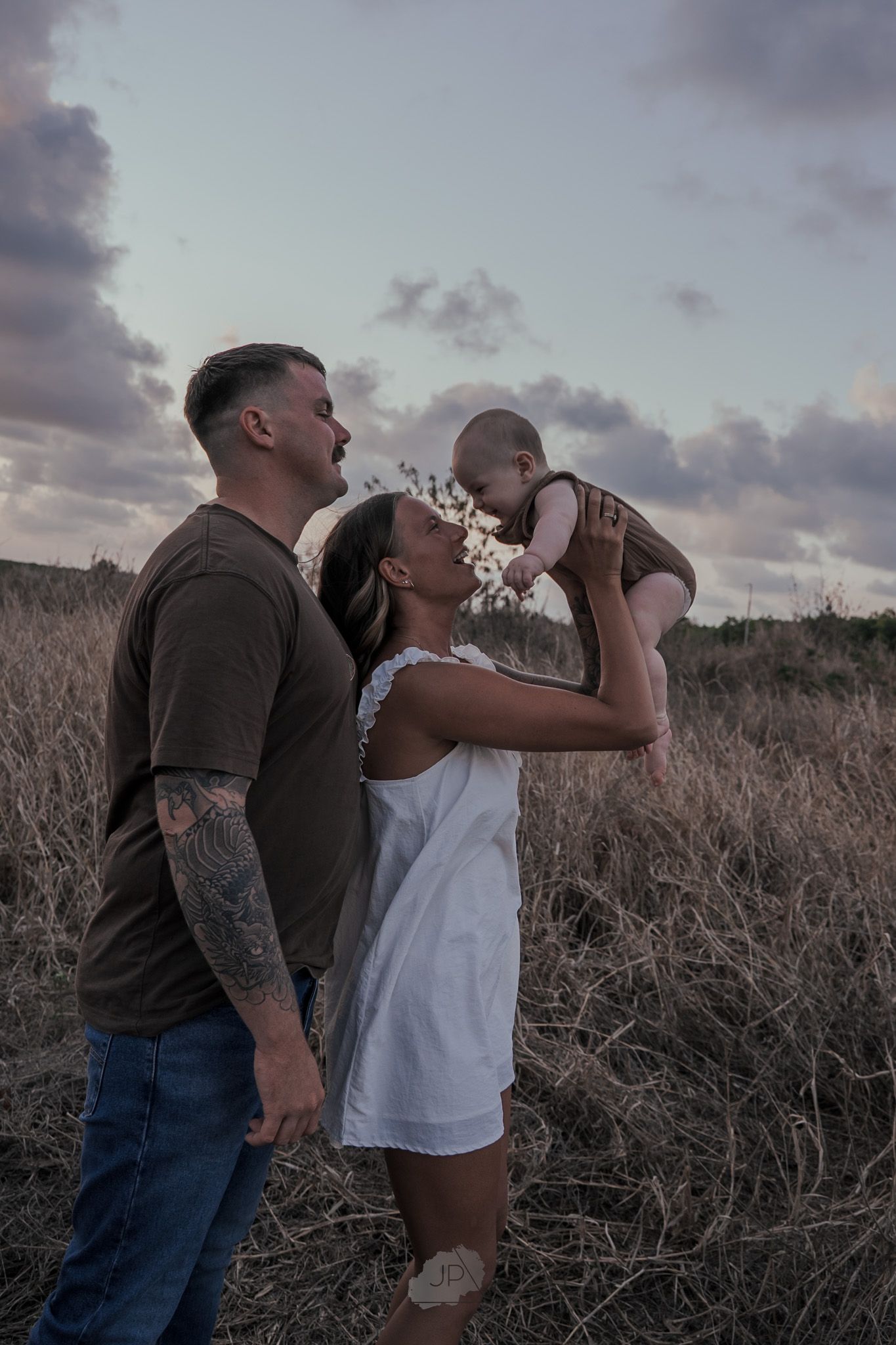 Two people share a playful moment together in a field at sunset, laughing and interacting with each other.