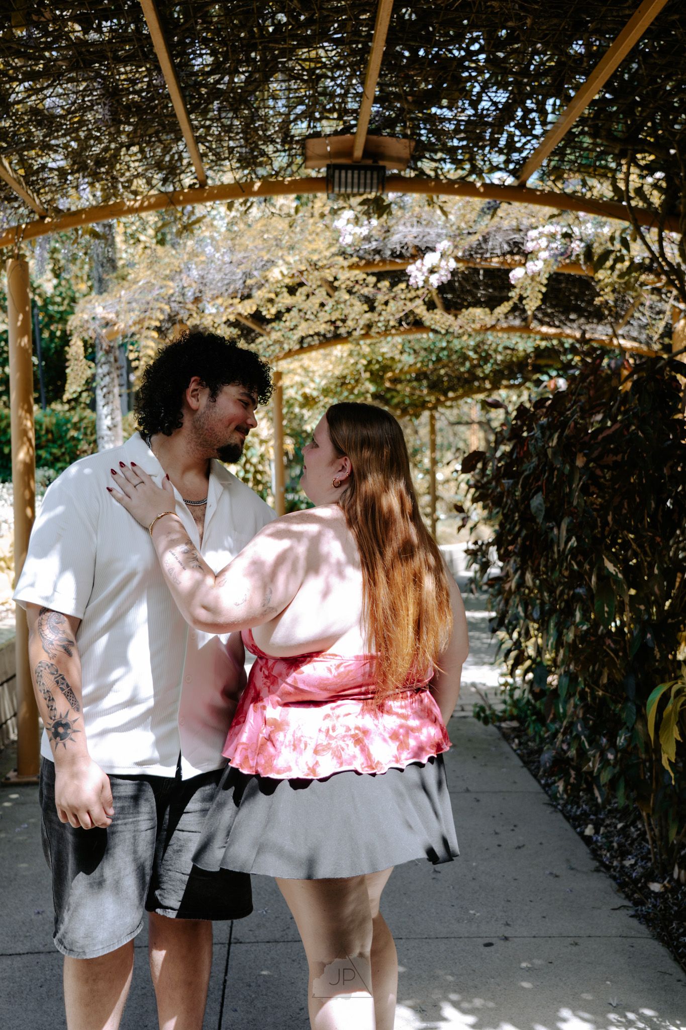 A couple dancing together in a garden pathway with trees and greenery in the background.