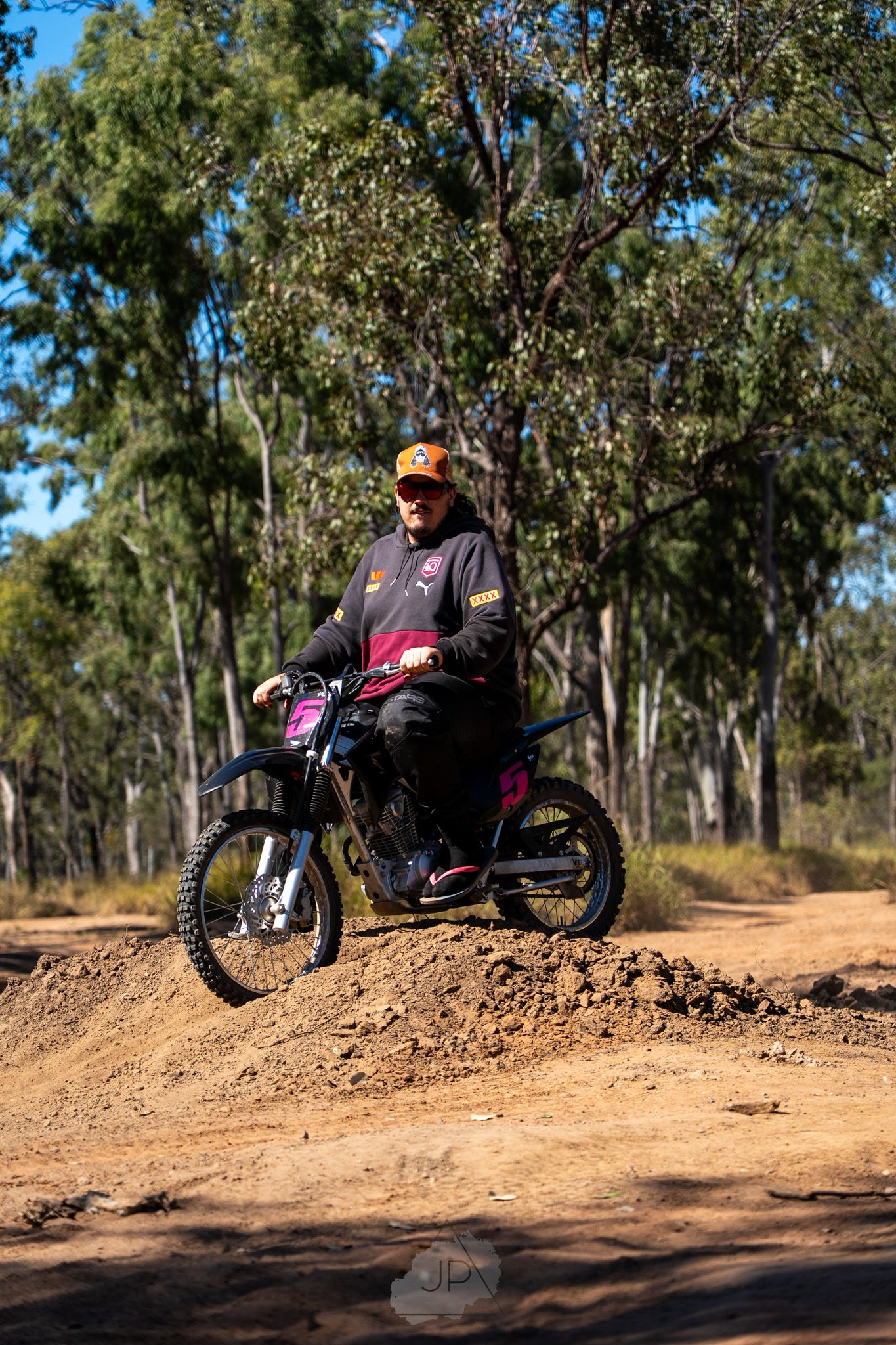 Sequence of motorcycle trick shots showing rider performing progressive jumps over dirt mounds in a wooded area.