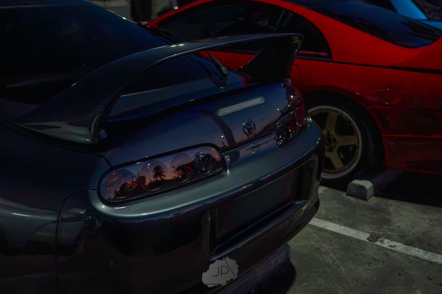 Row of shiny sports cars displayed in a dimly lit garage or showroom with red accent lighting.