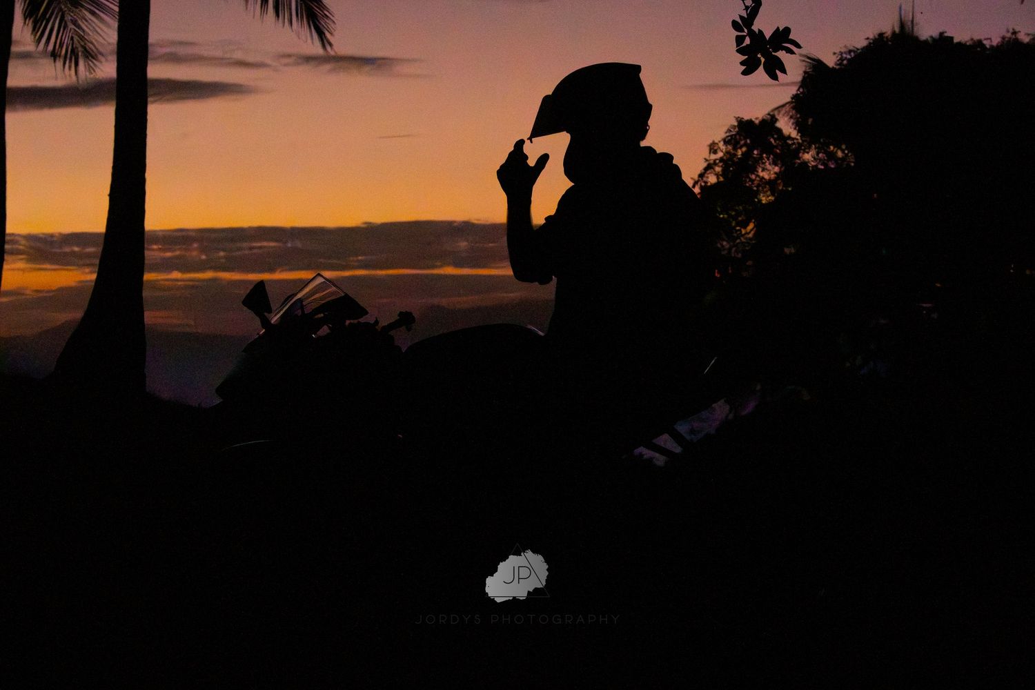 Silhouettes of palm trees frame a dramatic orange and purple sunset sky over a tropical coastline.