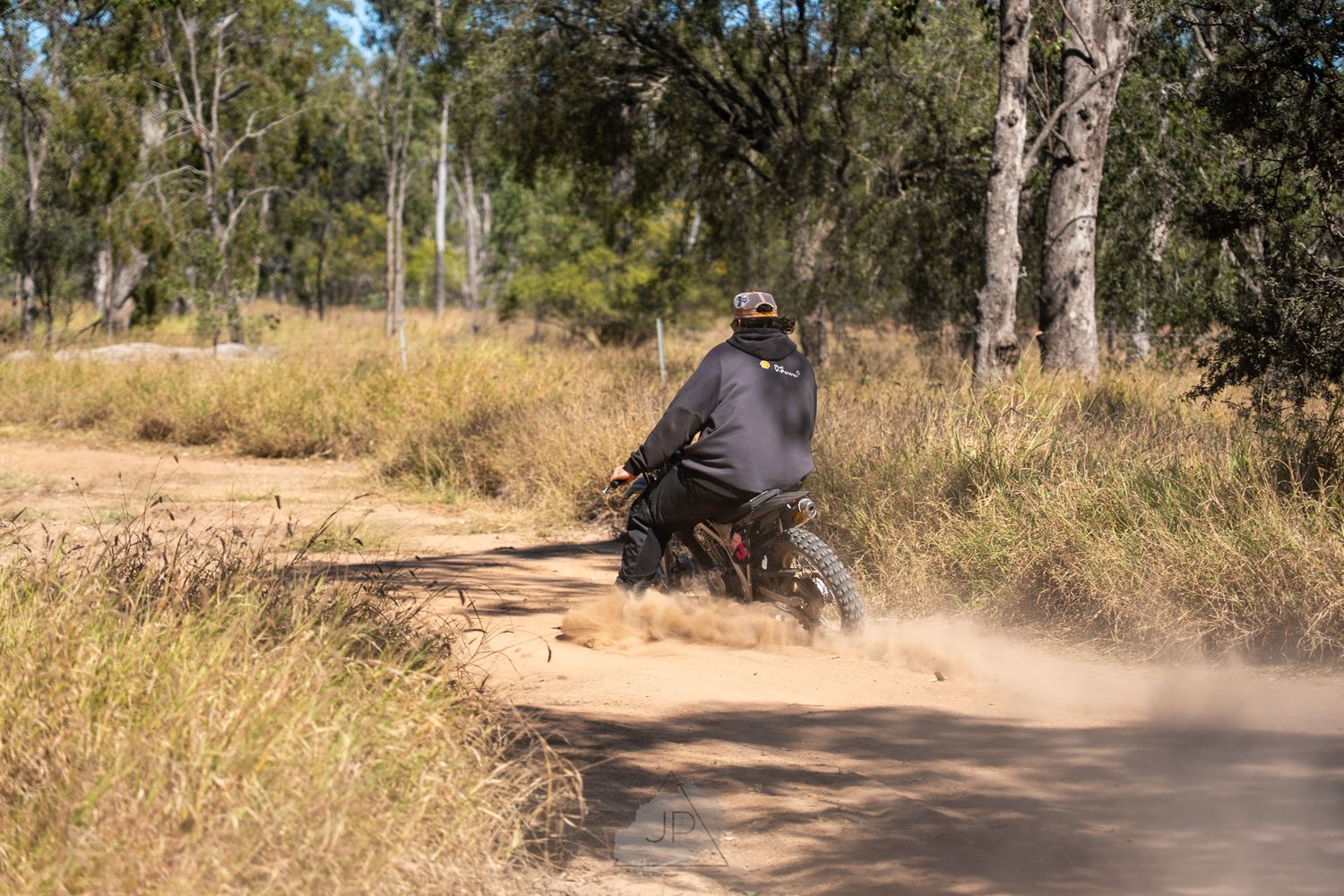 Mountain biker kicks up dust while riding on a dirt trail through eucalyptus trees on a sunny day.