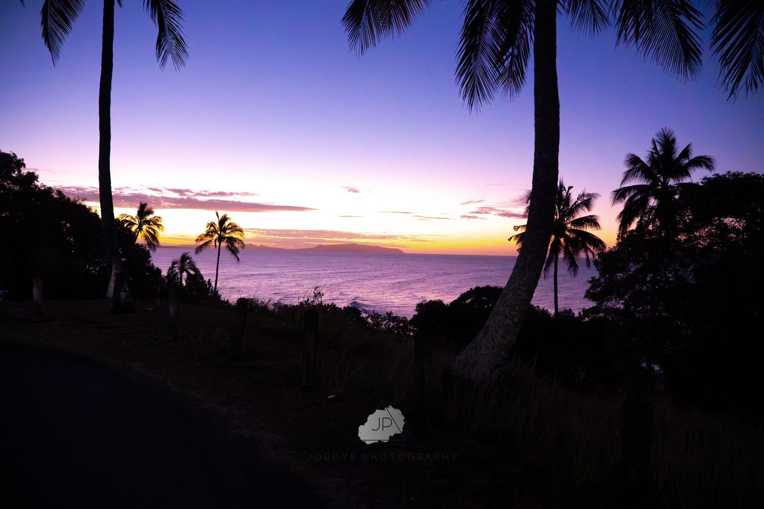 Stunning panorama of tropical palm trees silhouetted against a vibrant purple and orange sunset sky over Hawaii.