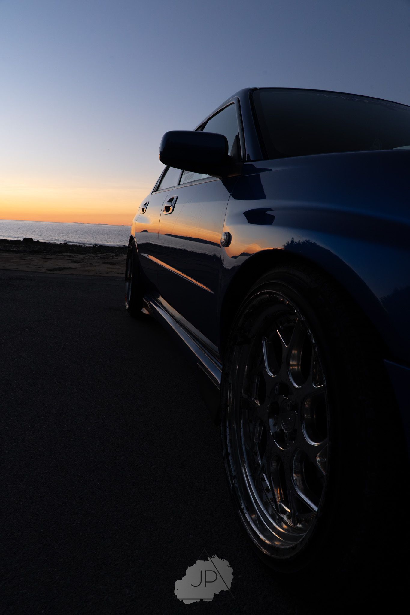 A Subaru sports car silhouetted against a sunset sky, showcasing its sleek profile and polished chrome wheels.