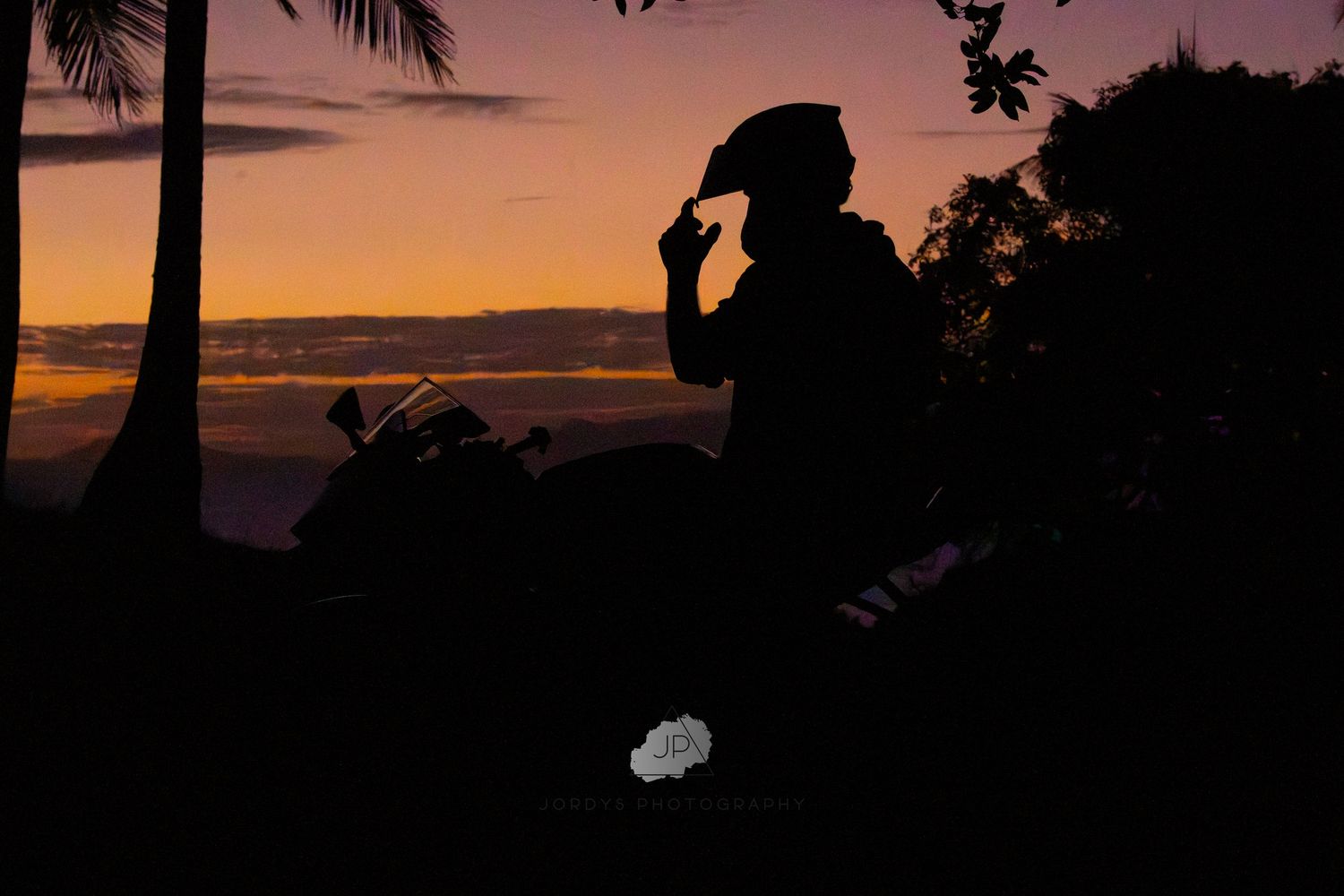 Silhouette of someone wearing a cowboy hat against a tropical sunset with palm trees.