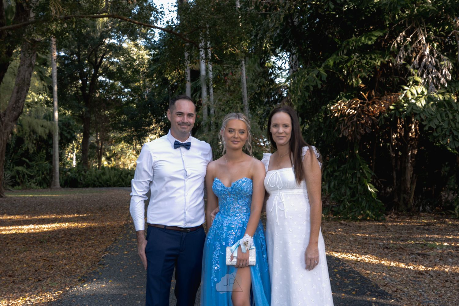 A wedding party poses outdoors in formal attire with bridesmaids in bright blue dresses and groomsmen in navy suits.