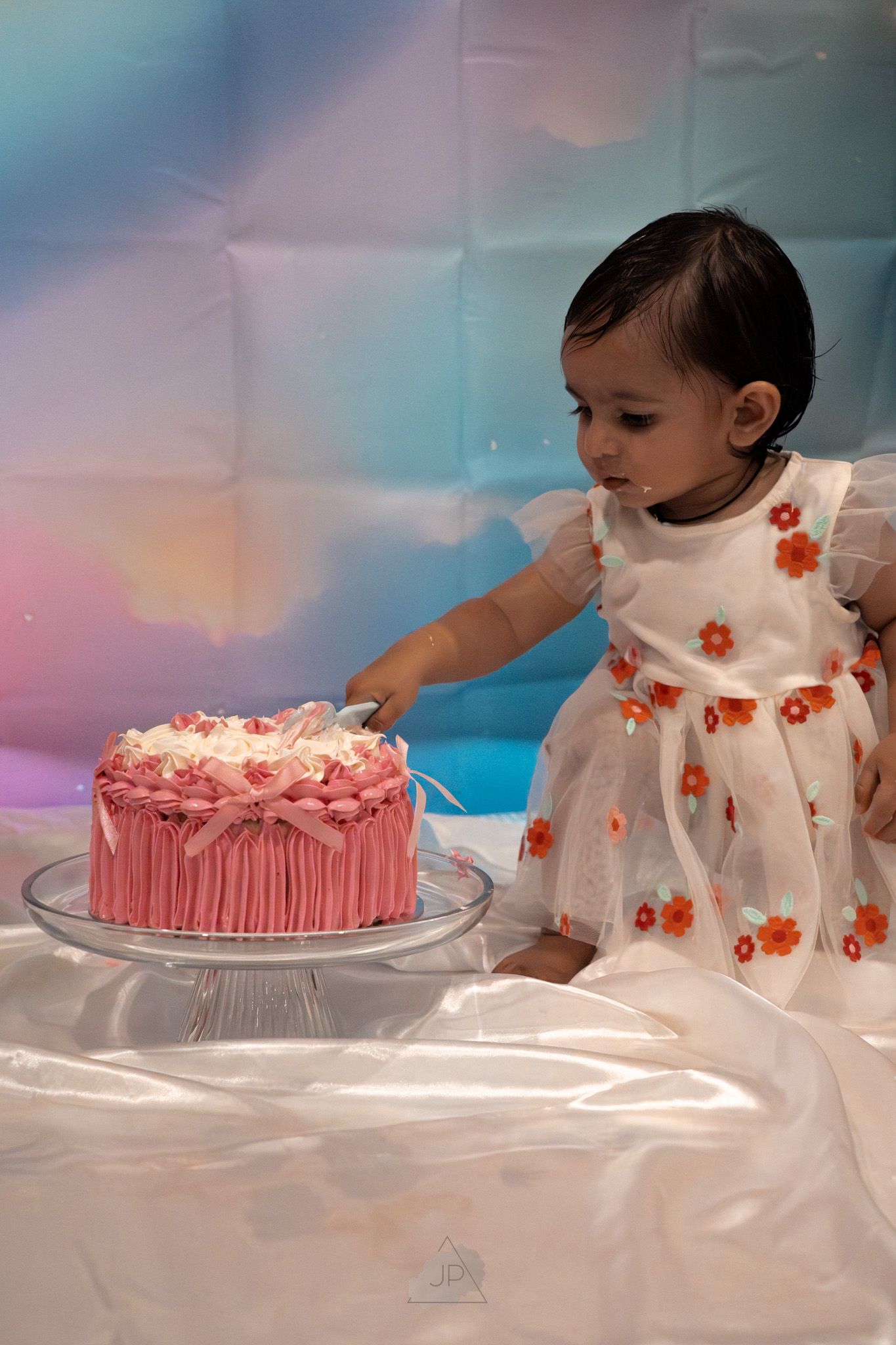 A beautifully decorated pink cake sits on a glass cake stand against a dreamy pastel background.