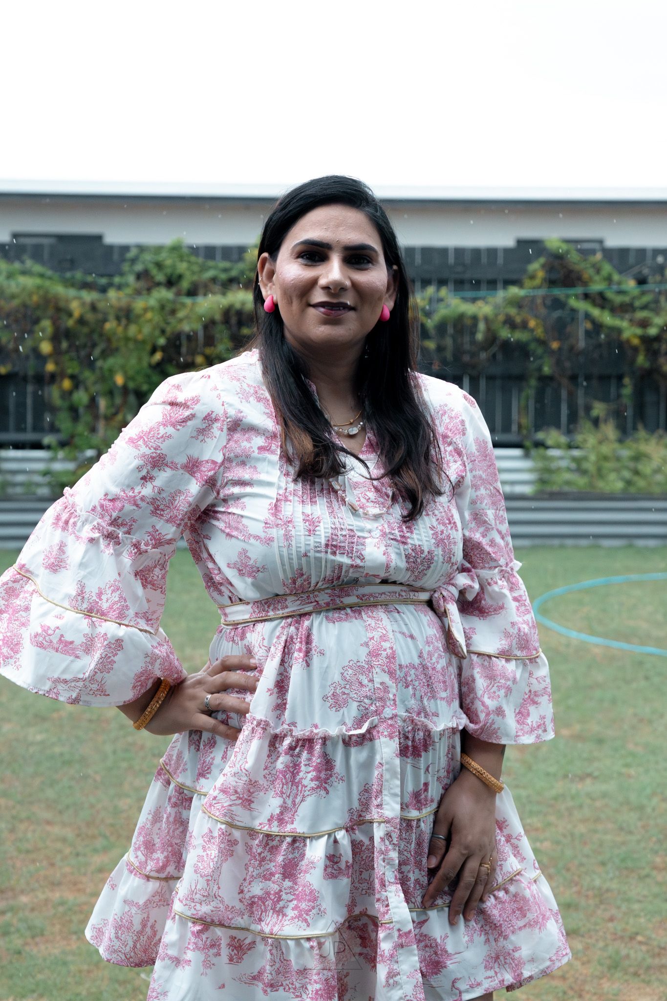 A person poses outdoors in a flowing white and pink floral dress with ruffled tiers and puff sleeves.