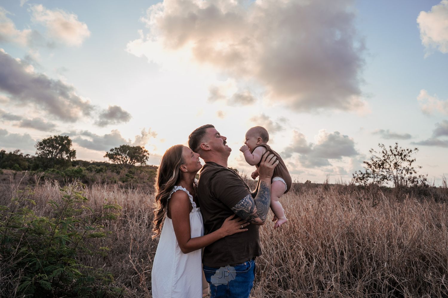 A couple shares an intimate moment in a field of tall grass during golden hour sunset.