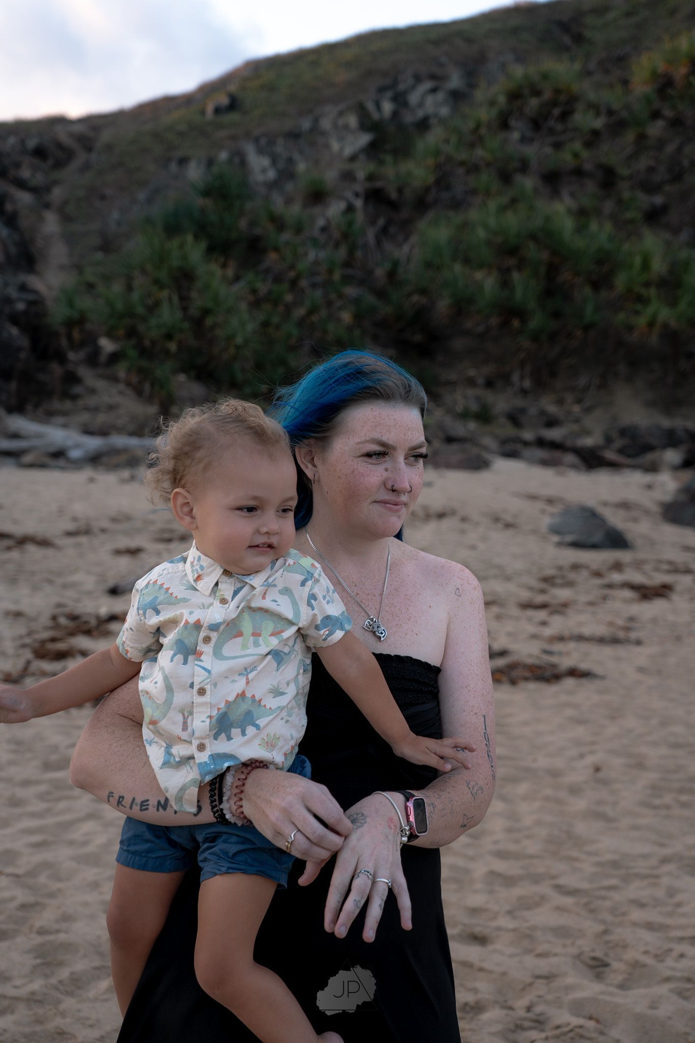 A parent and toddler share a tender moment together on a sandy beach with mountains in the background.