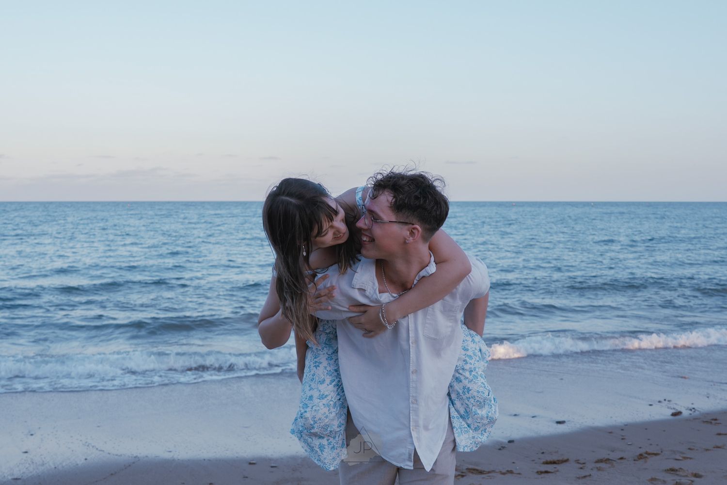A romantic couple embraces on the beach at sunset with the ocean waves rolling in behind them.