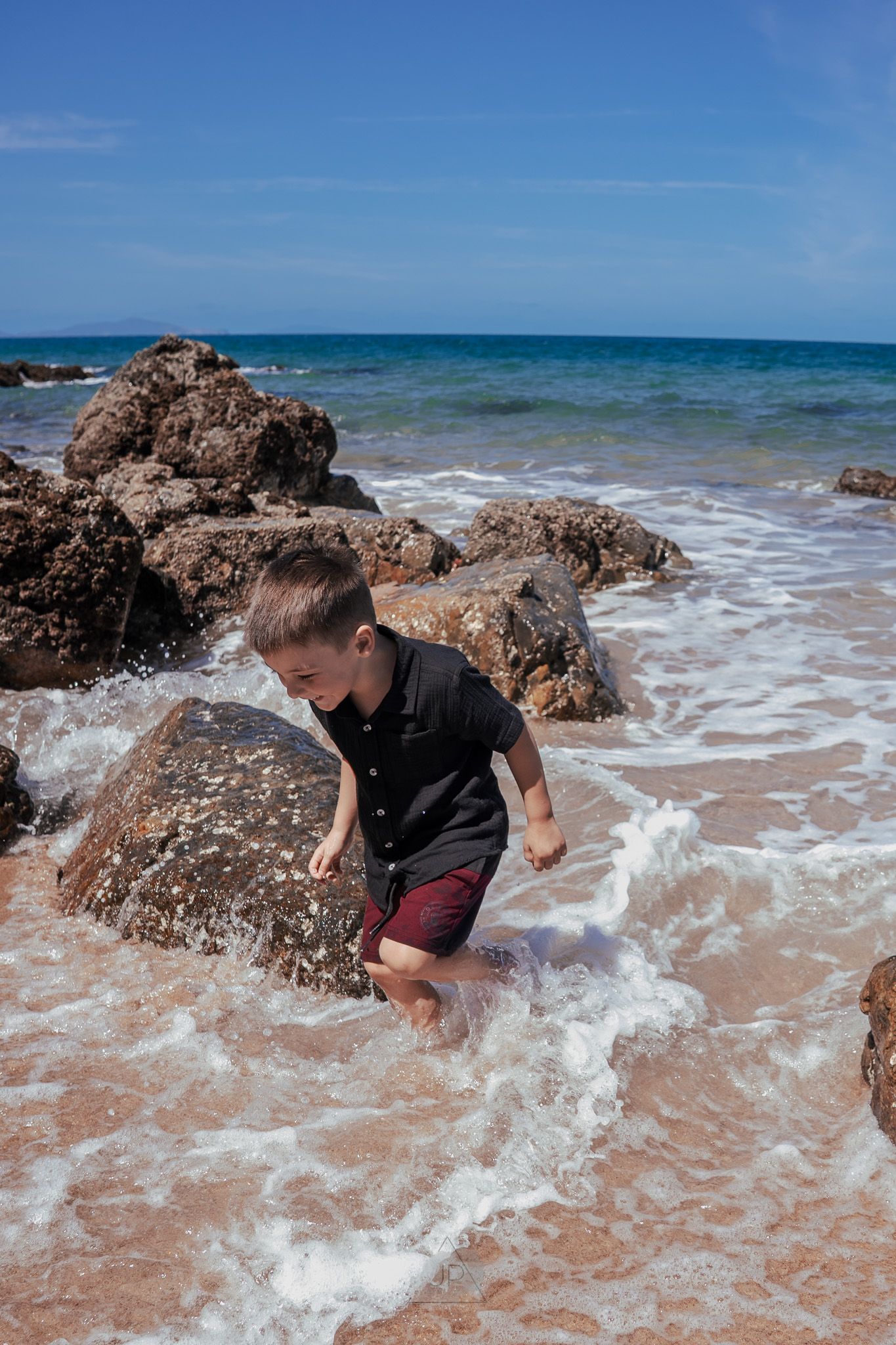 A sequence of photos showing someone playing in ocean waves crashing against rocky outcrops on a sunny beach.