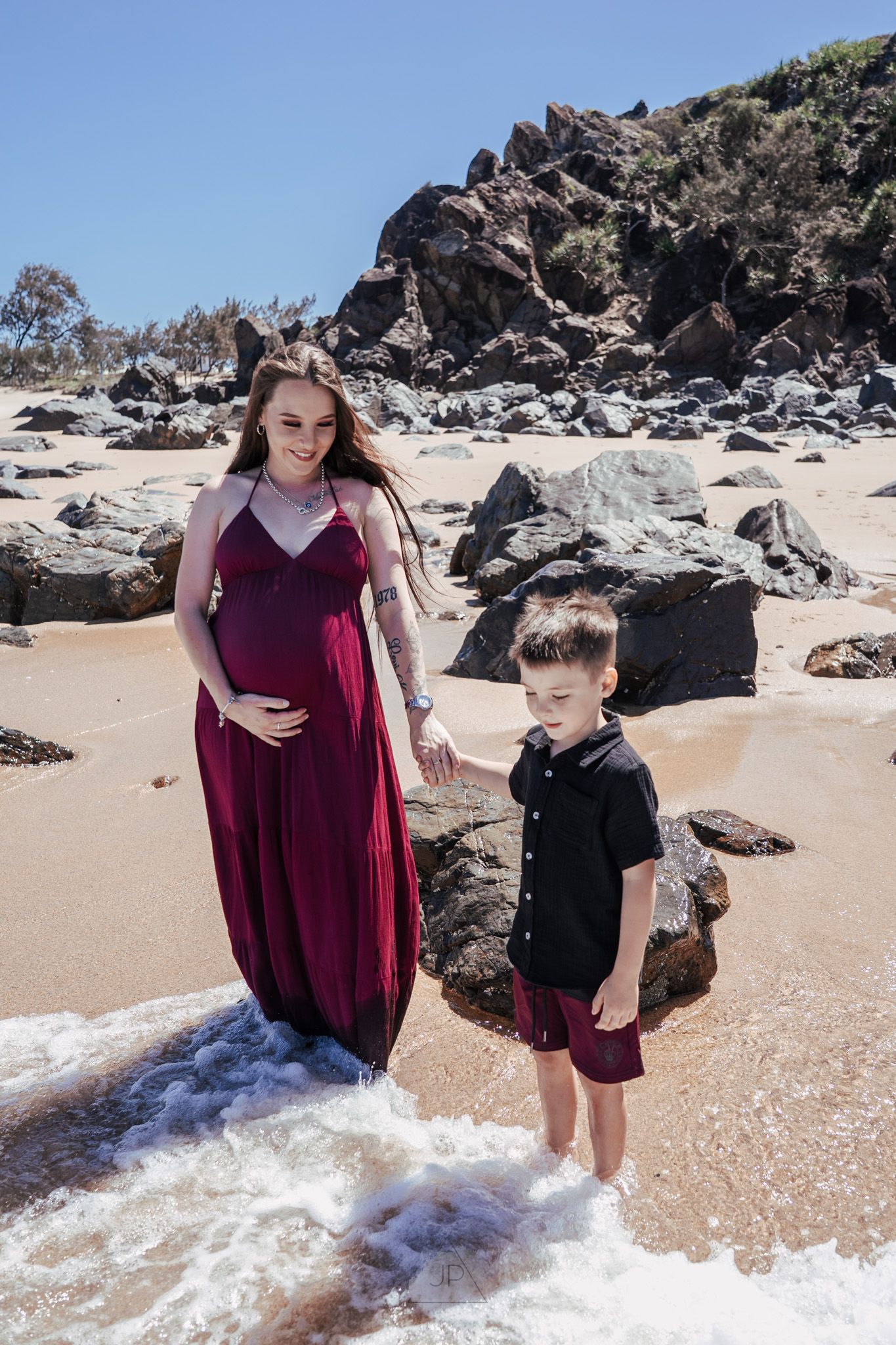 A family enjoys the waves crashing on a rocky beach with volcanic formations in the background.