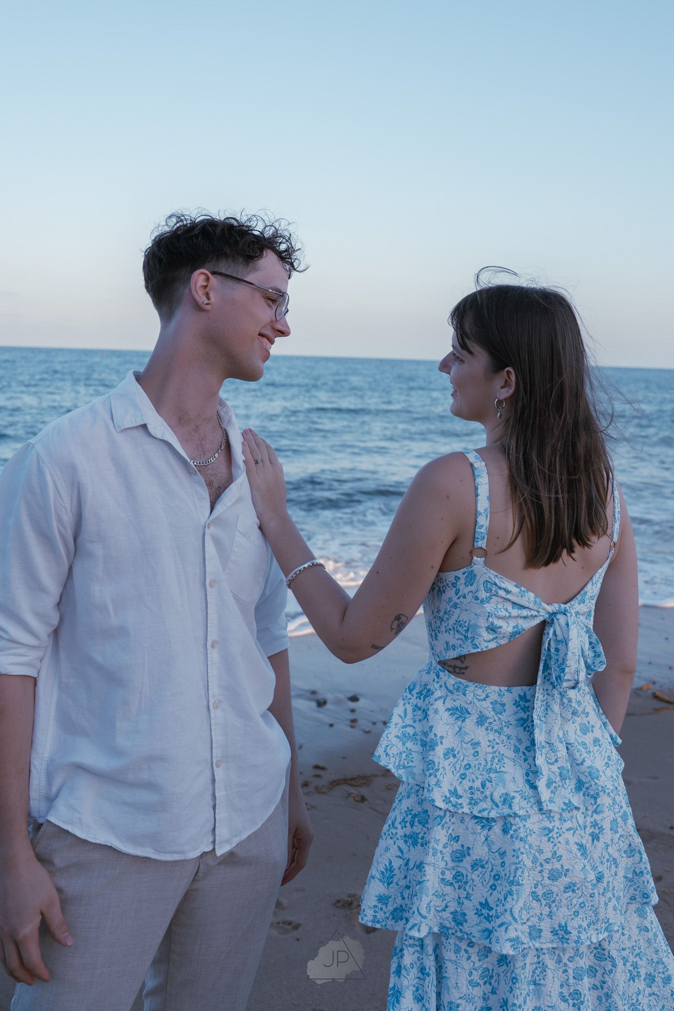 A couple in beachwear shares playful moments along the shoreline at sunset.