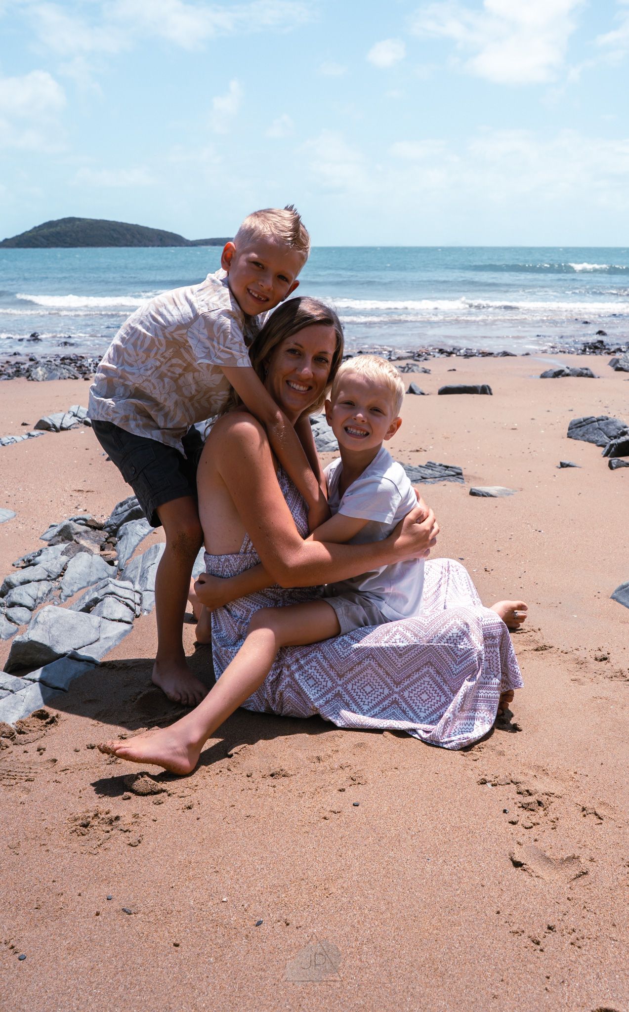 A couple shares a playful moment while relaxing on a blanket at a sunny beach with ocean waves in the background.