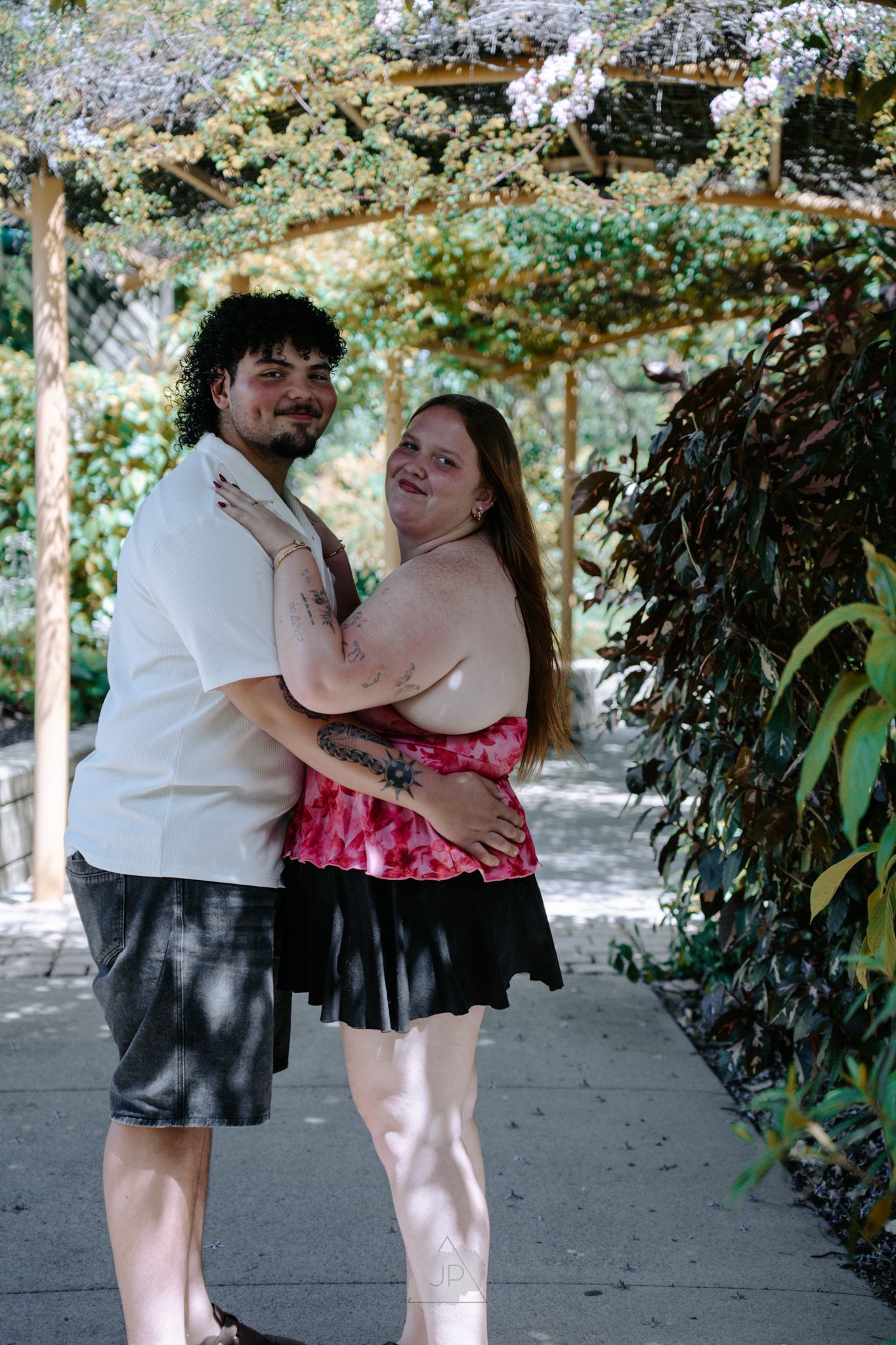 A couple dances together under a leafy garden pergola in a series of candid romantic moments.