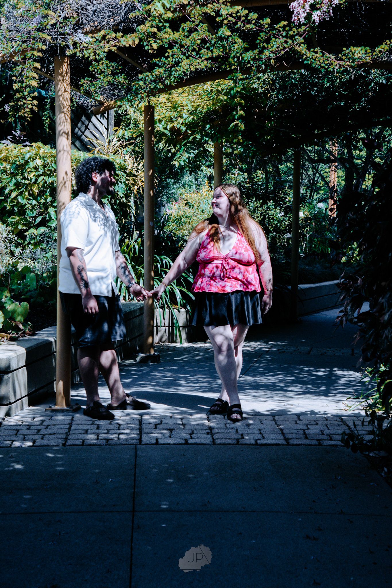 A sequence of people walking up stone steps on a shaded garden path surrounded by lush green trees and foliage.
