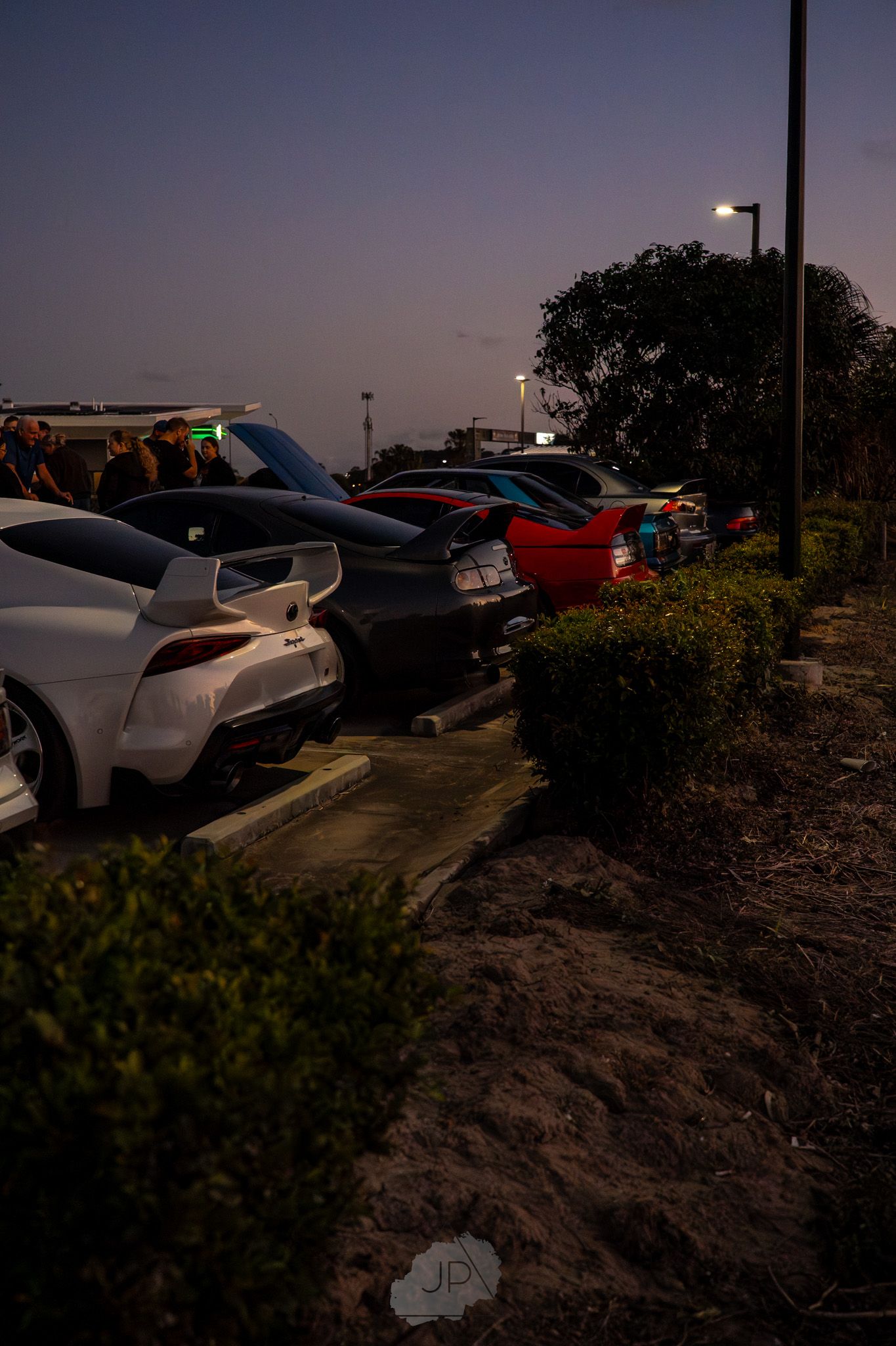 A series of parked cars at sunset with a dramatic view of the landscape and sky in golden hour lighting.