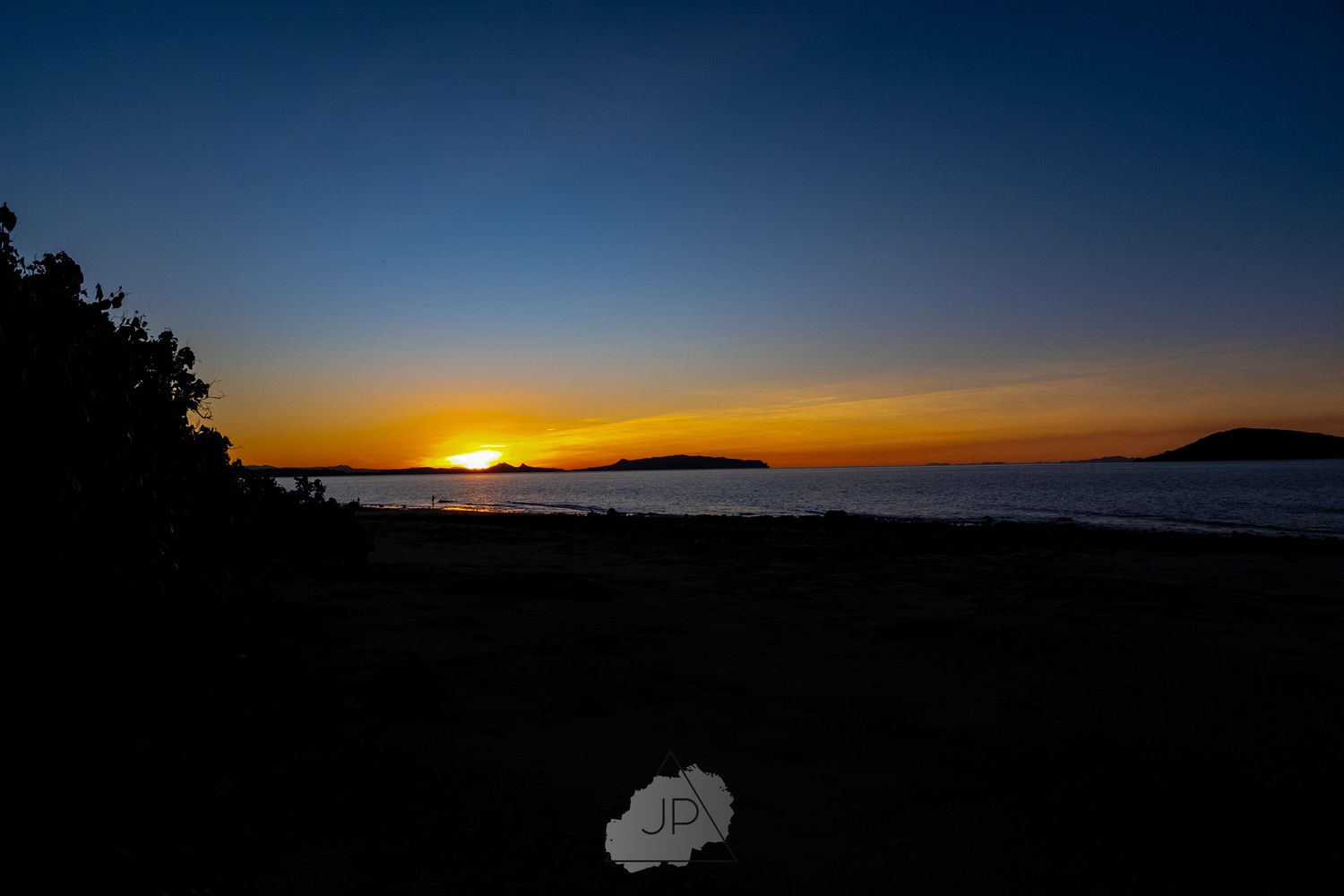 Dramatic coastal sunset with silhouetted islands on the horizon creating a golden sky over the ocean.