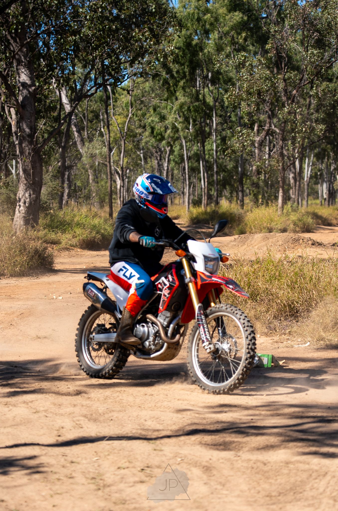 Orange dirt bike parked on dusty trail in bushland with tall eucalyptus trees in the background.