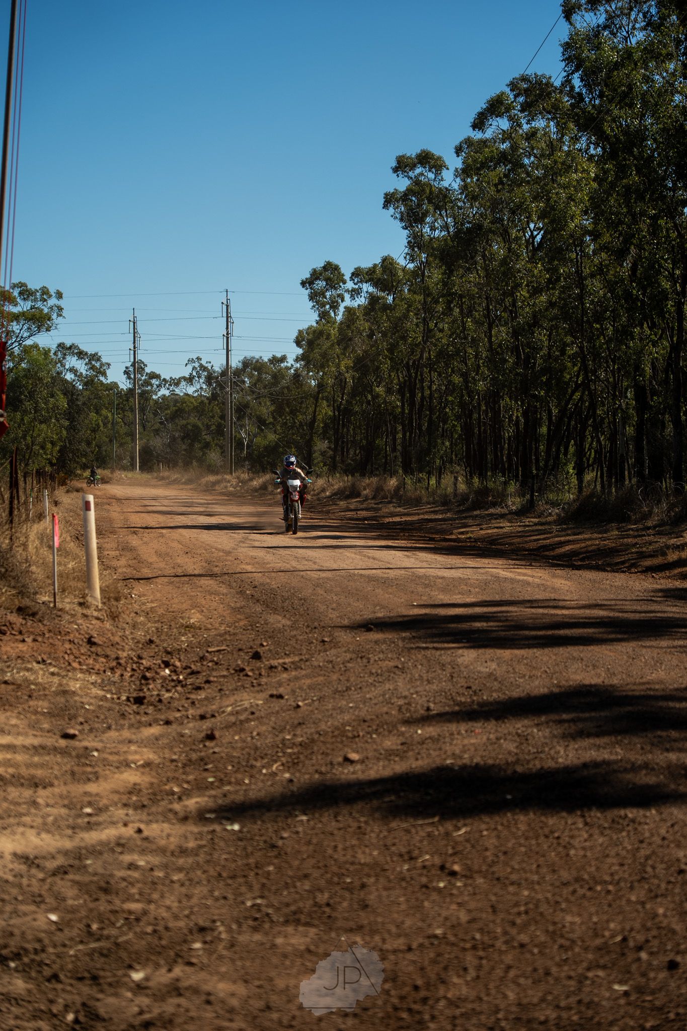 A dirt trail winding through a wooded area with utility poles visible in the distance.