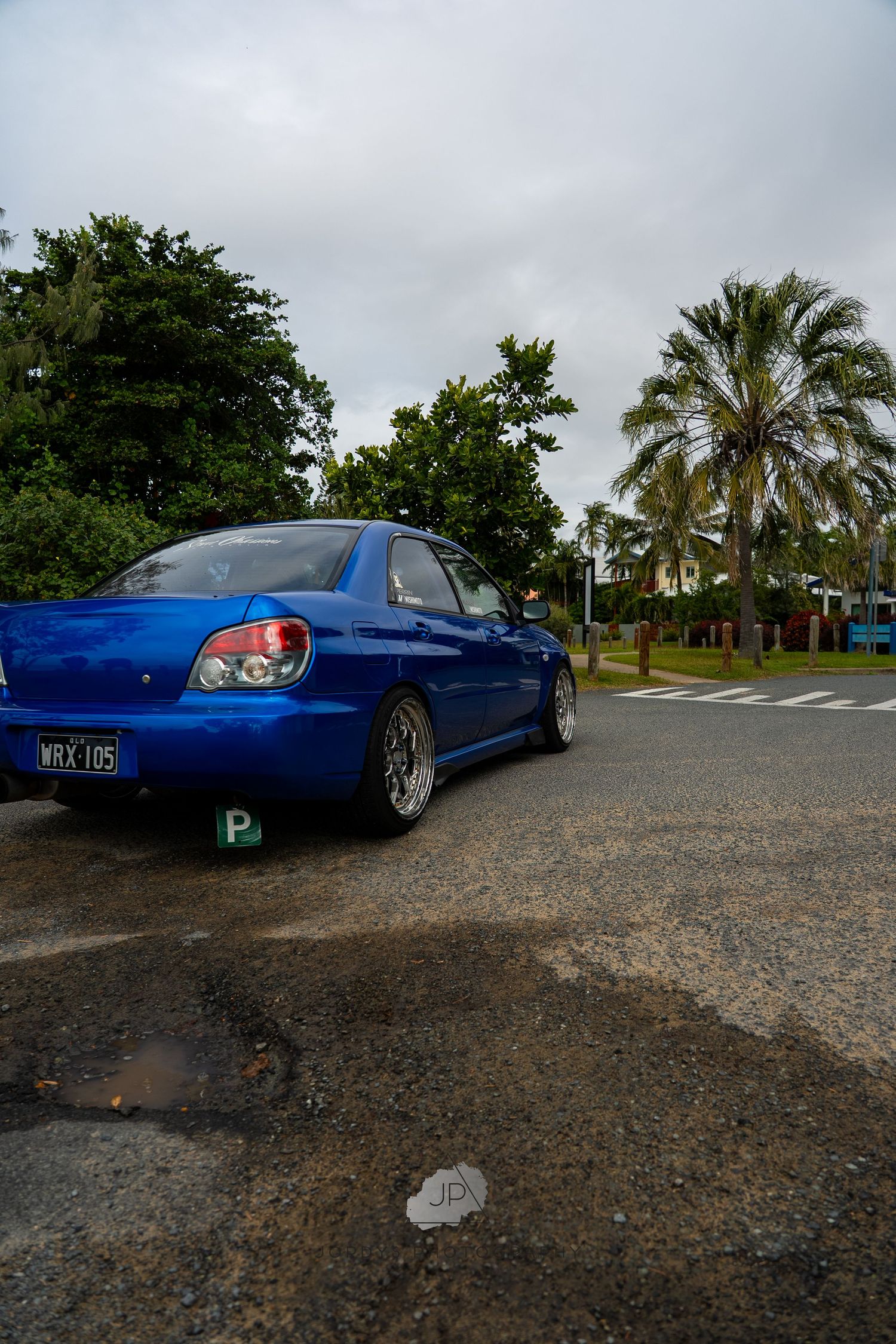 Low-angle shots of a modified blue Nissan R33 Skyline GT-R parked on gravel with palm trees in background.
