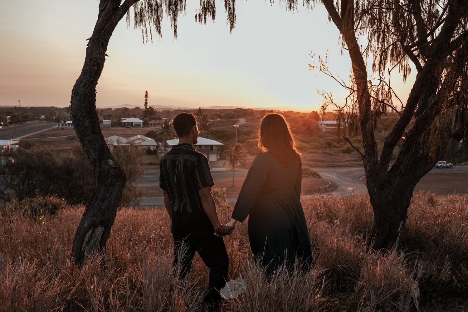Silhouettes of a couple standing together against a glowing sunset backdrop in a rustic outdoor setting.