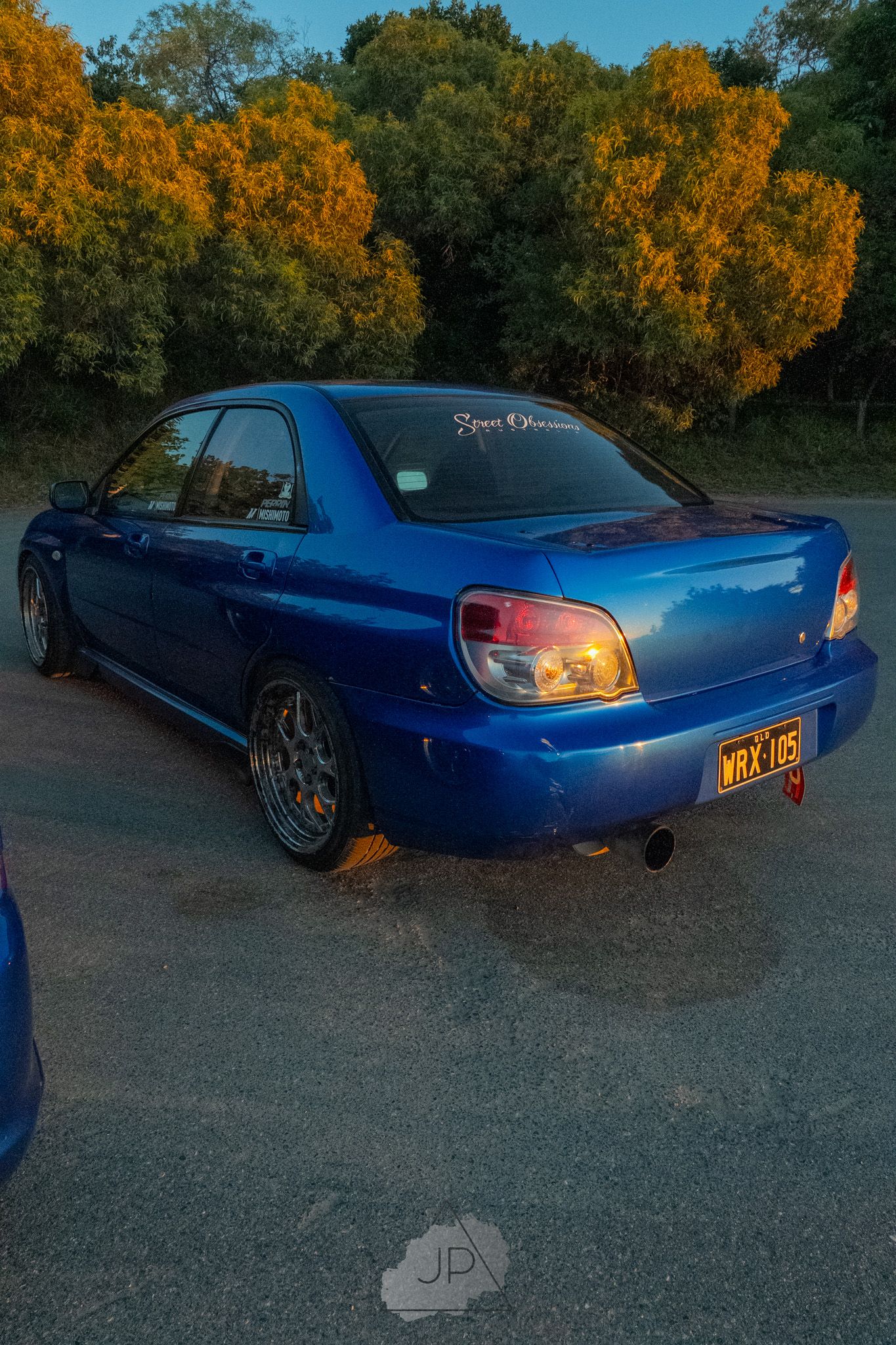 Blue JDM modified Japanese sports car at sunset against bright autumn foliage.