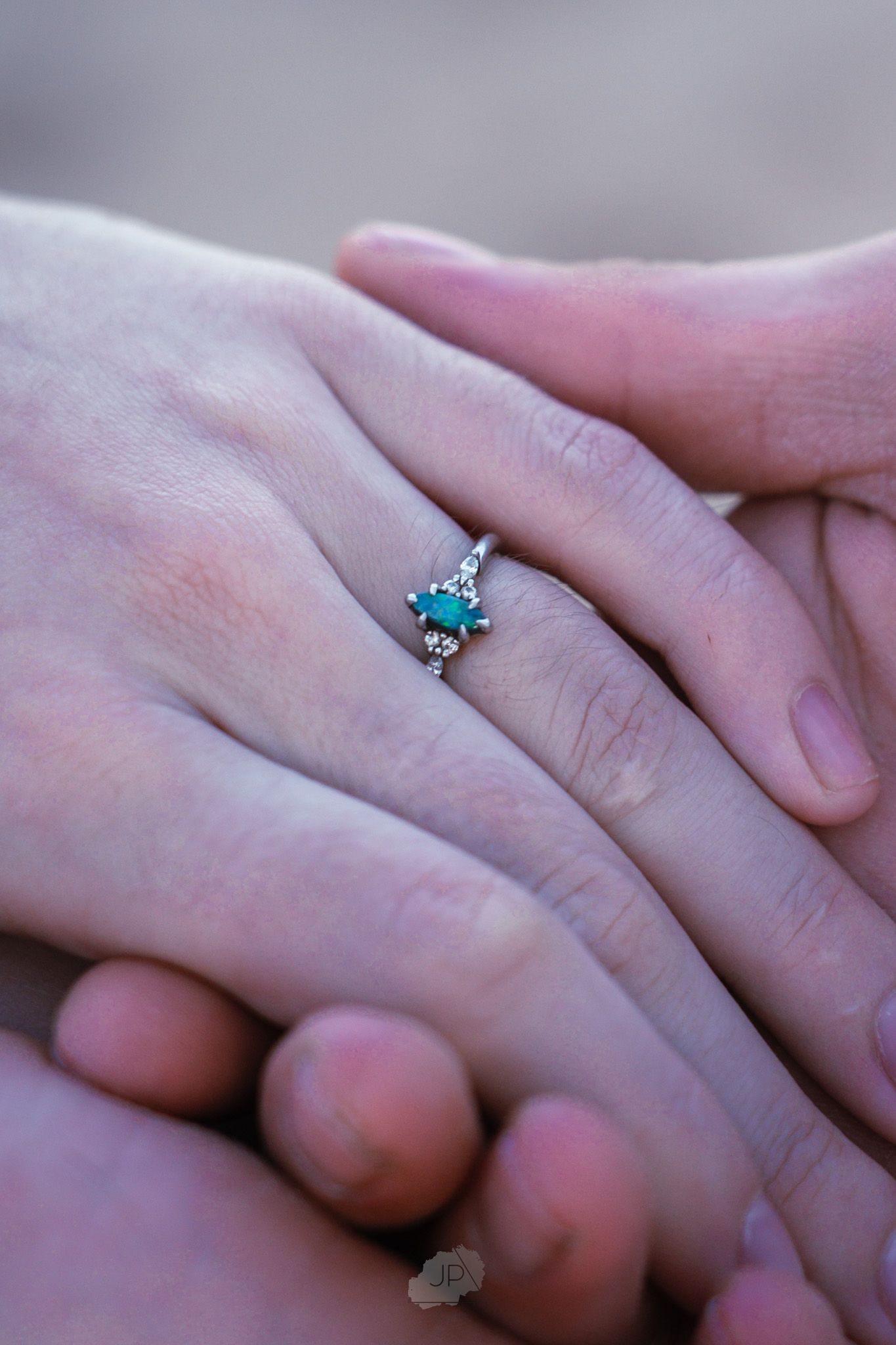 Close-up of hands showing an engagement ring with a turquoise stone in a delicate setting.