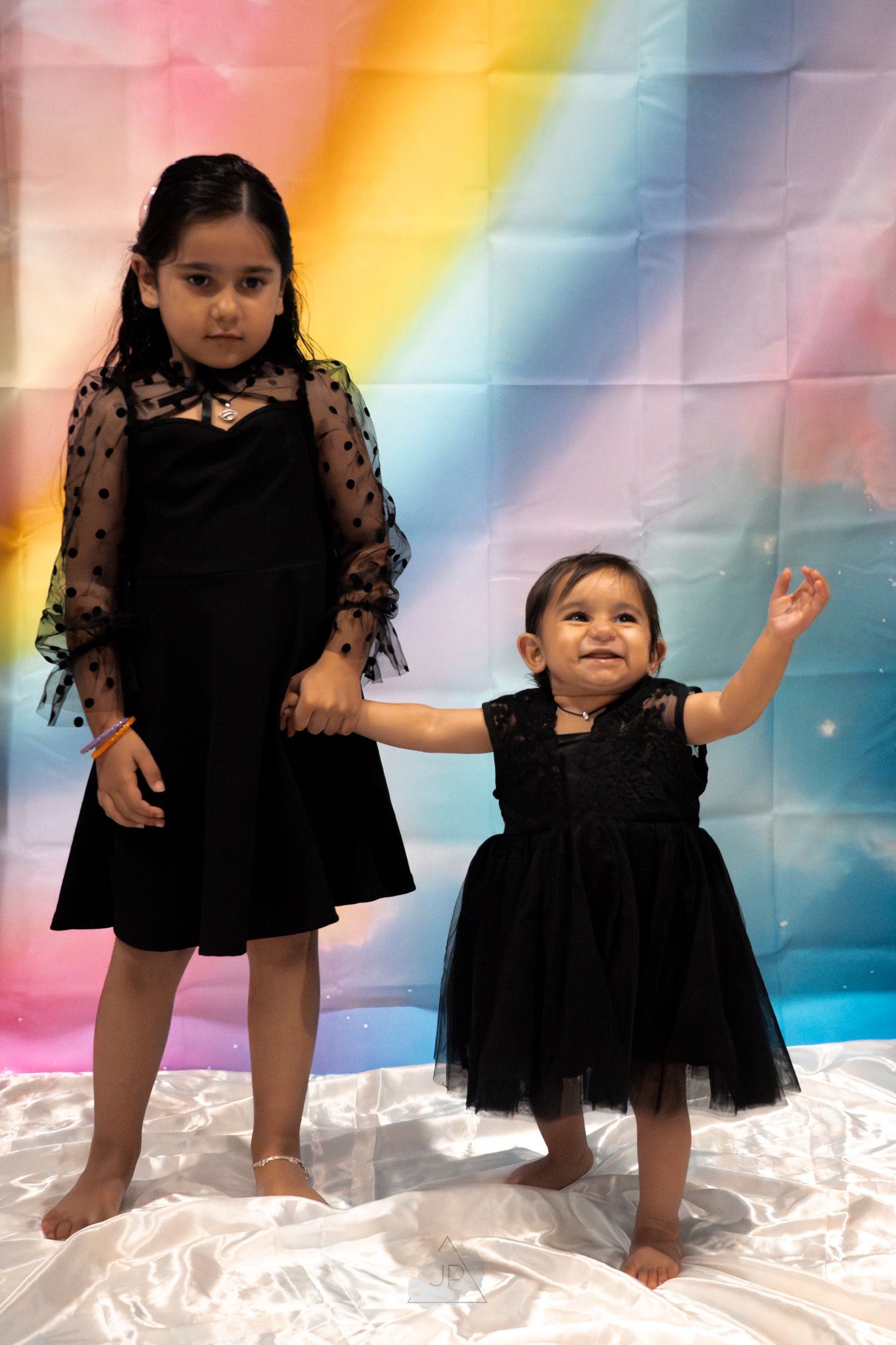 A series of five photos showing a child in a black tulle dress posing playfully against a rainbow-colored background.