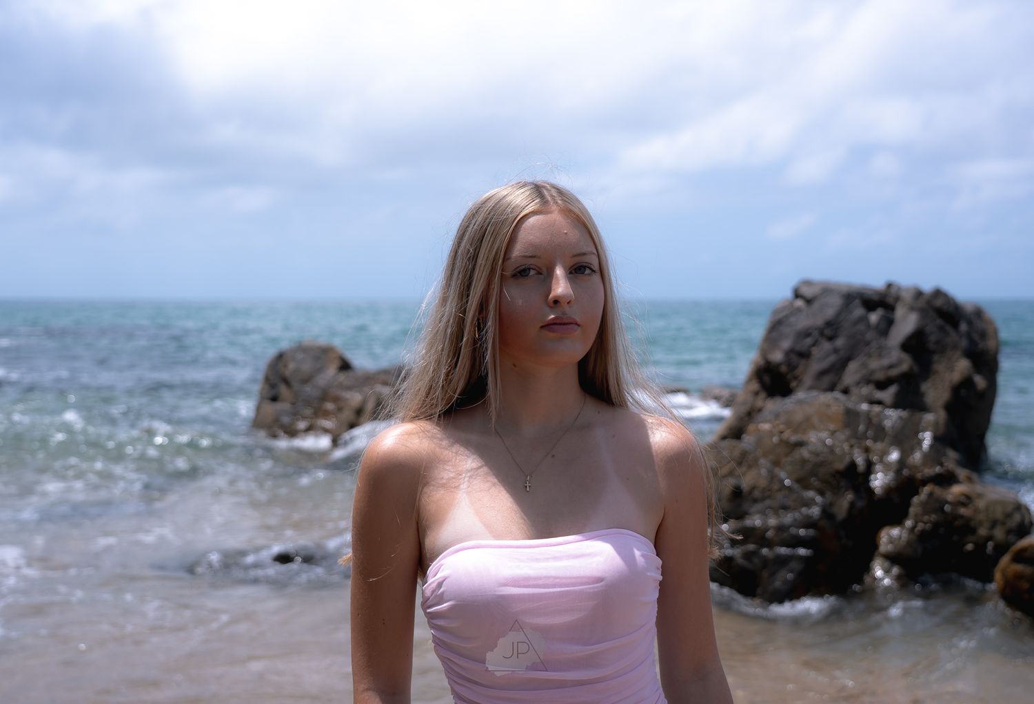 Someone in a pink swimsuit poses on a rocky beach with waves crashing in the background.