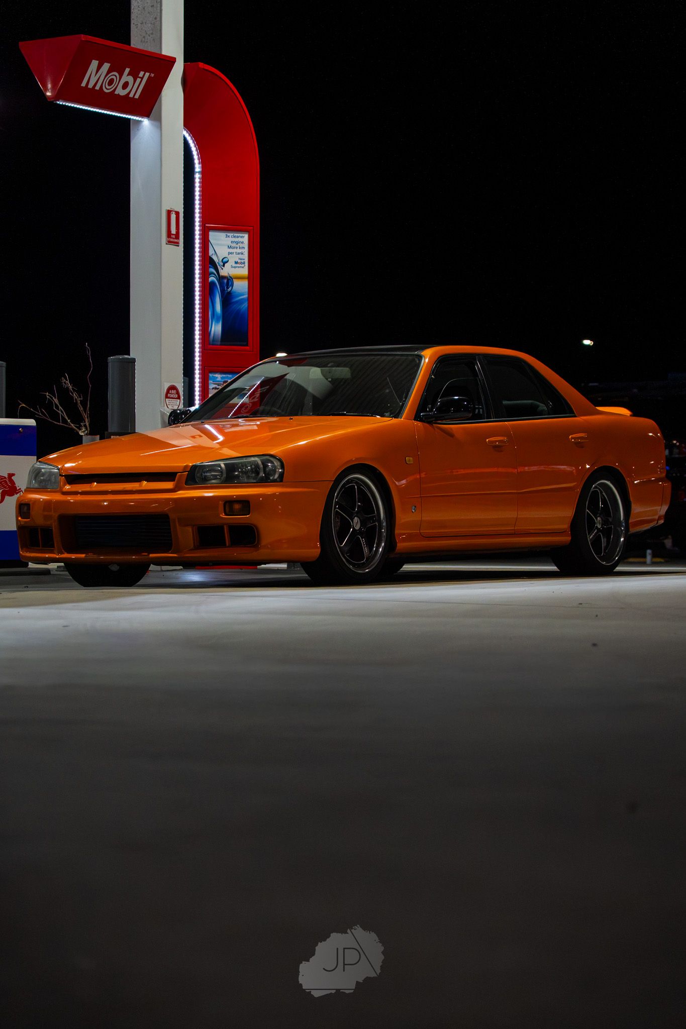 Orange Dodge Charger Daytona parked at night under red Mobil gas station lighting.