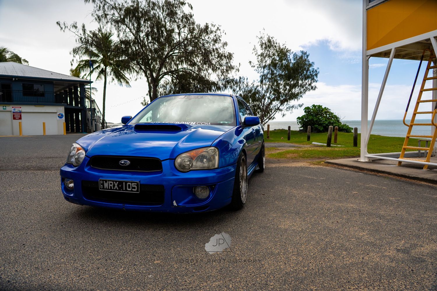A bright blue Subaru WRX STI sports car parked on a scenic roadway with trees in the background.
