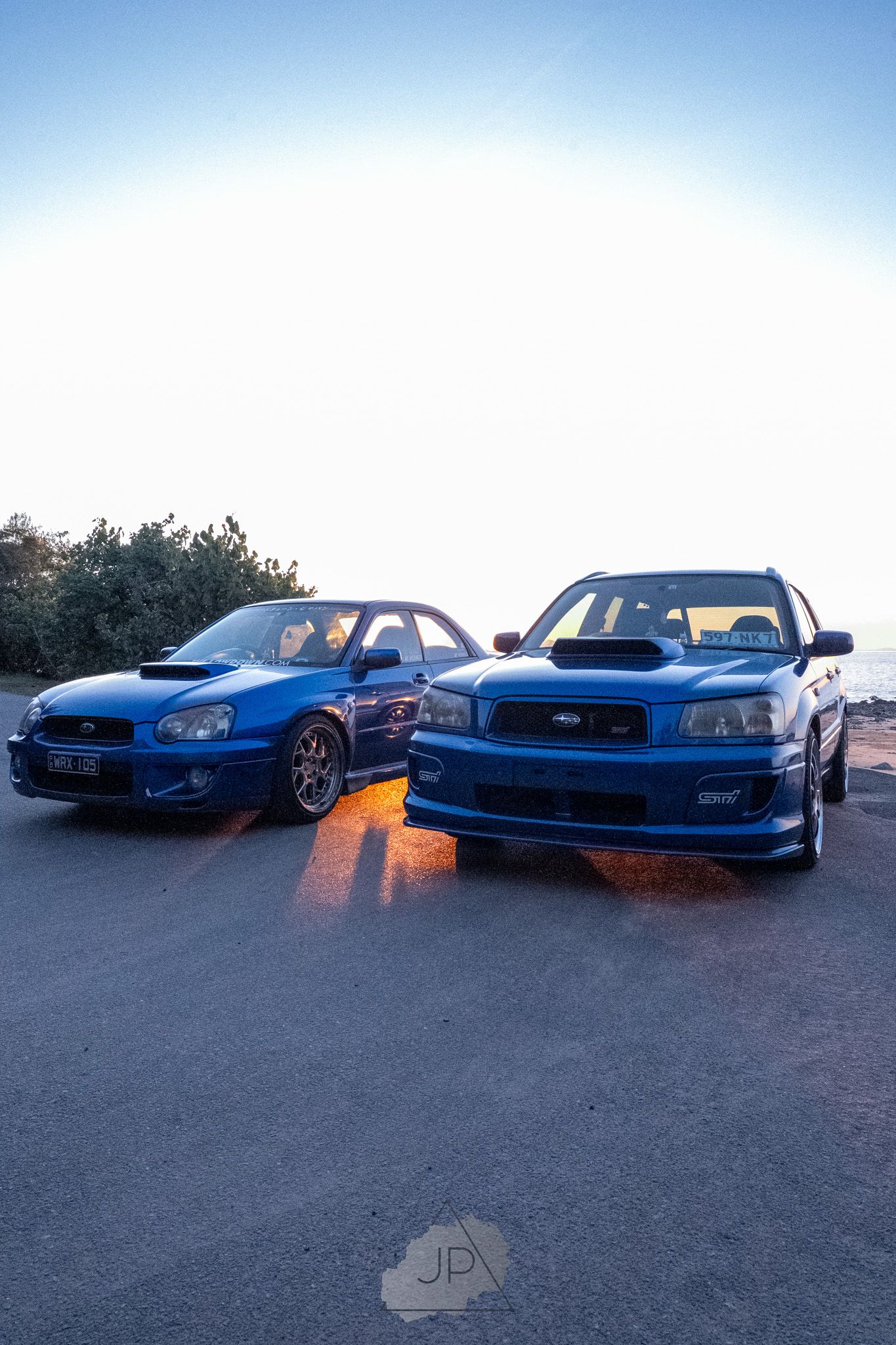 Four blue Subaru WRX sports cars parked in a line at sunset showcase their sleek profiles and modified styling.