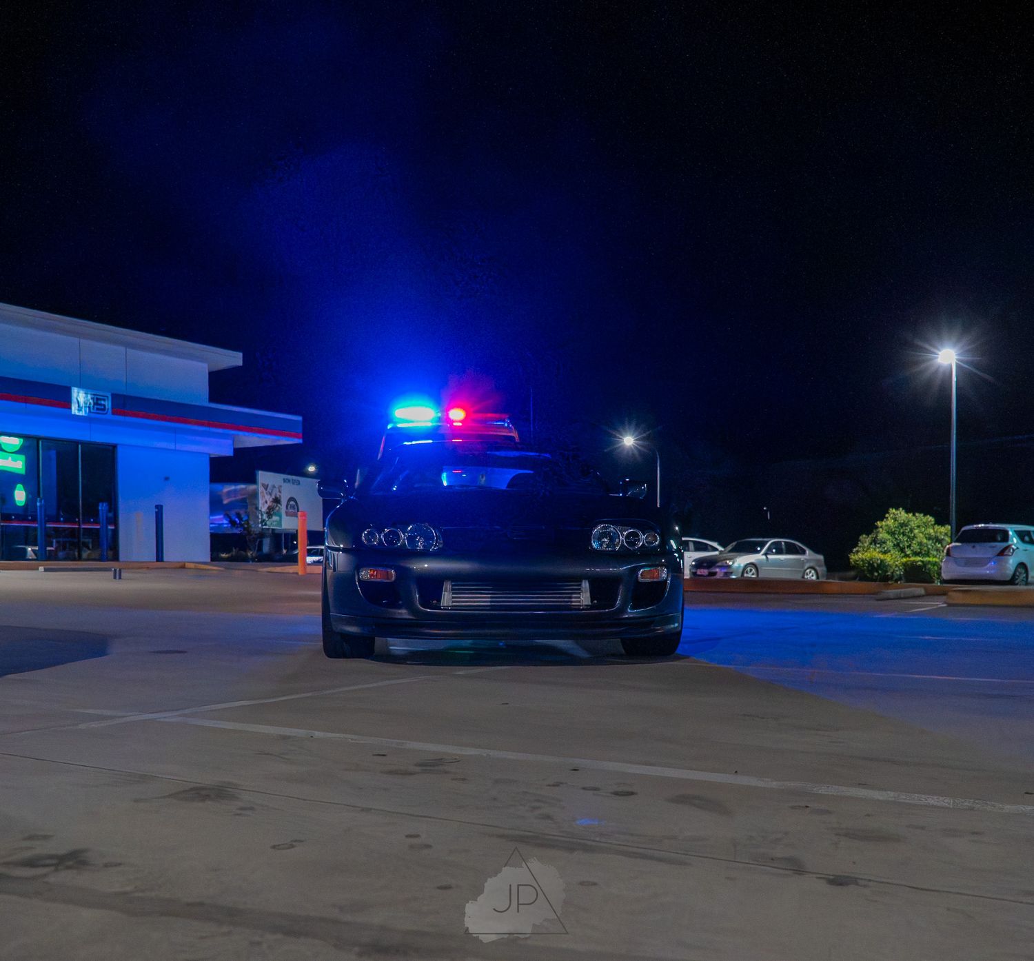 Emergency vehicles with flashing blue lights illuminate a dark parking lot at night with police cars visible.