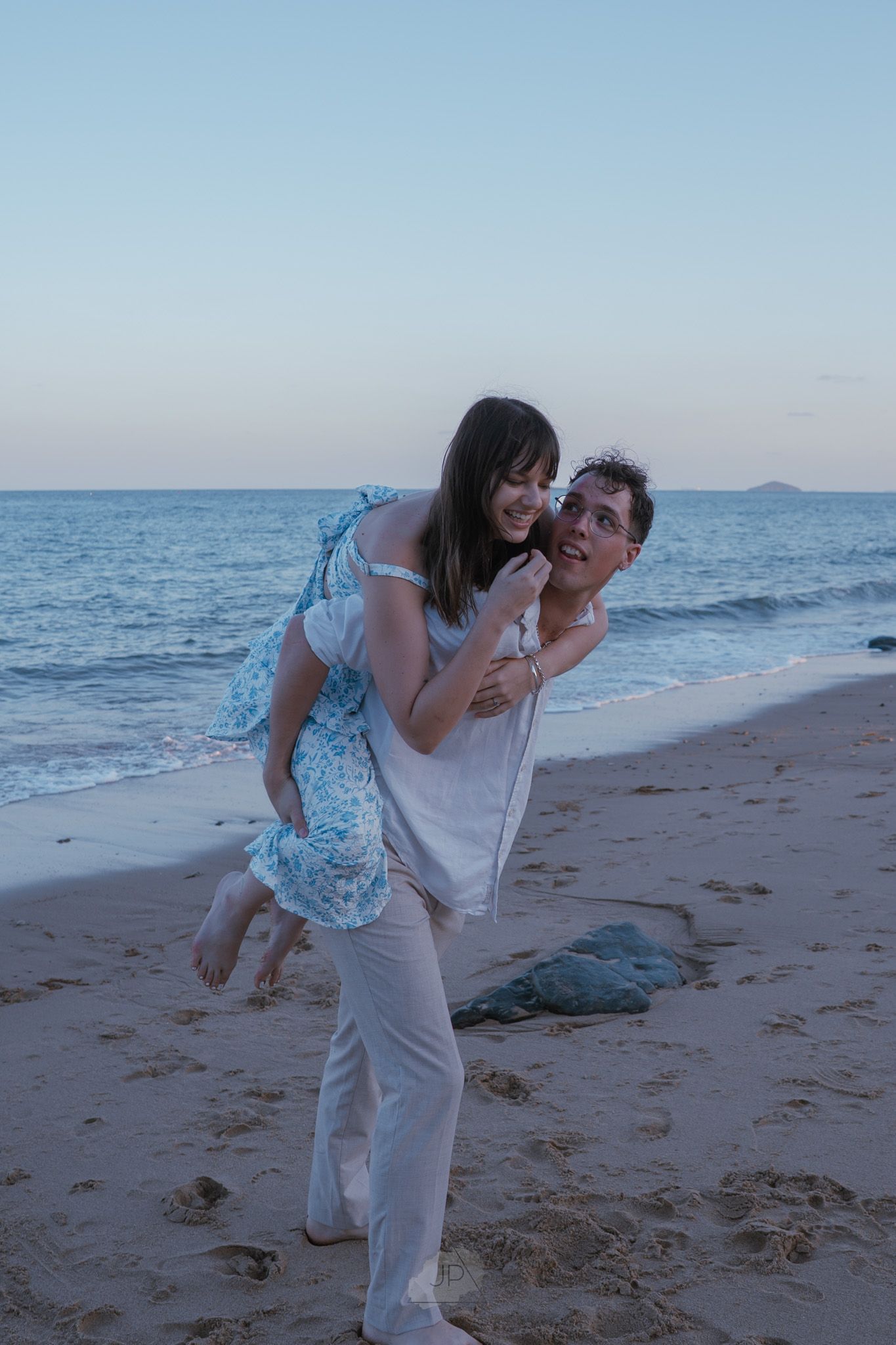 A playful couple shares a romantic moment on the beach at dusk with the ocean waves in the background.