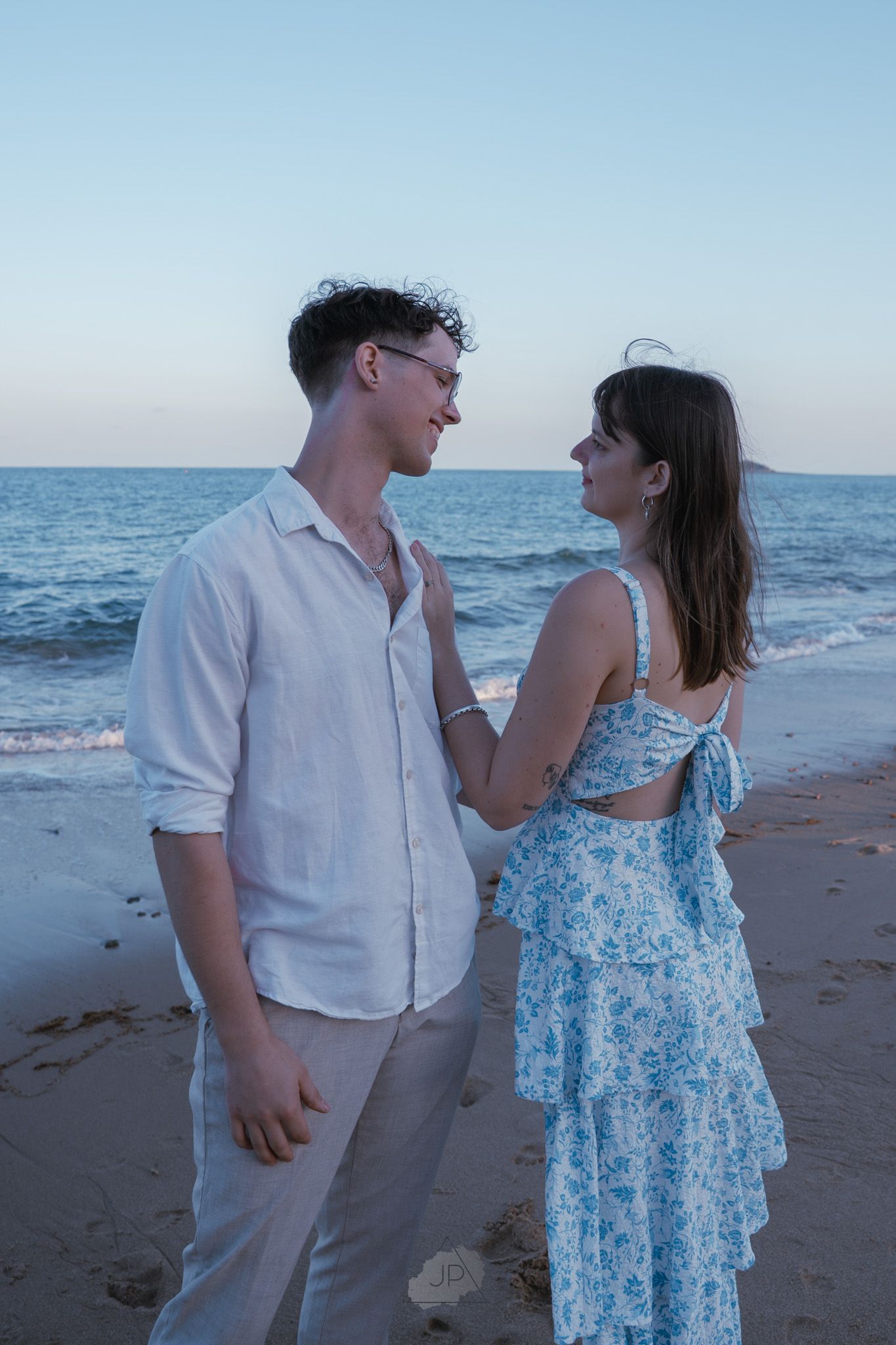 A couple in coordinating blue and white outfits share romantic moments on a beach at sunset.