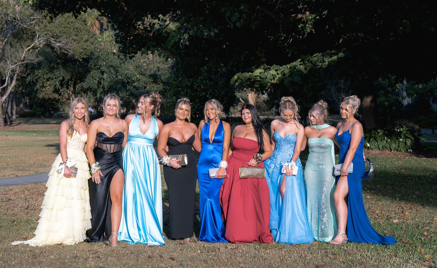 Group of people wearing formal attire in shades of blue and red pose together outdoors for photos.
