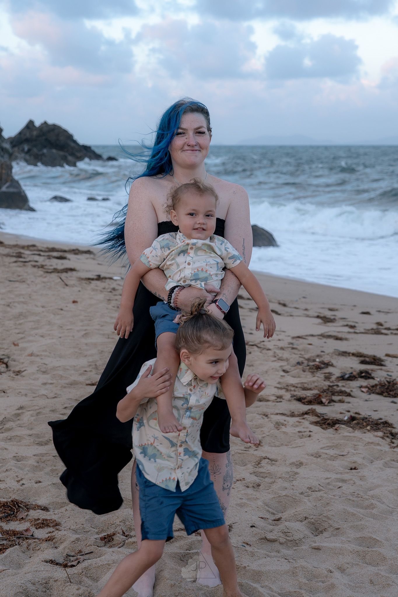 A playful moment captured on a cloudy beach with waves crashing against rocky outcrops in the background.