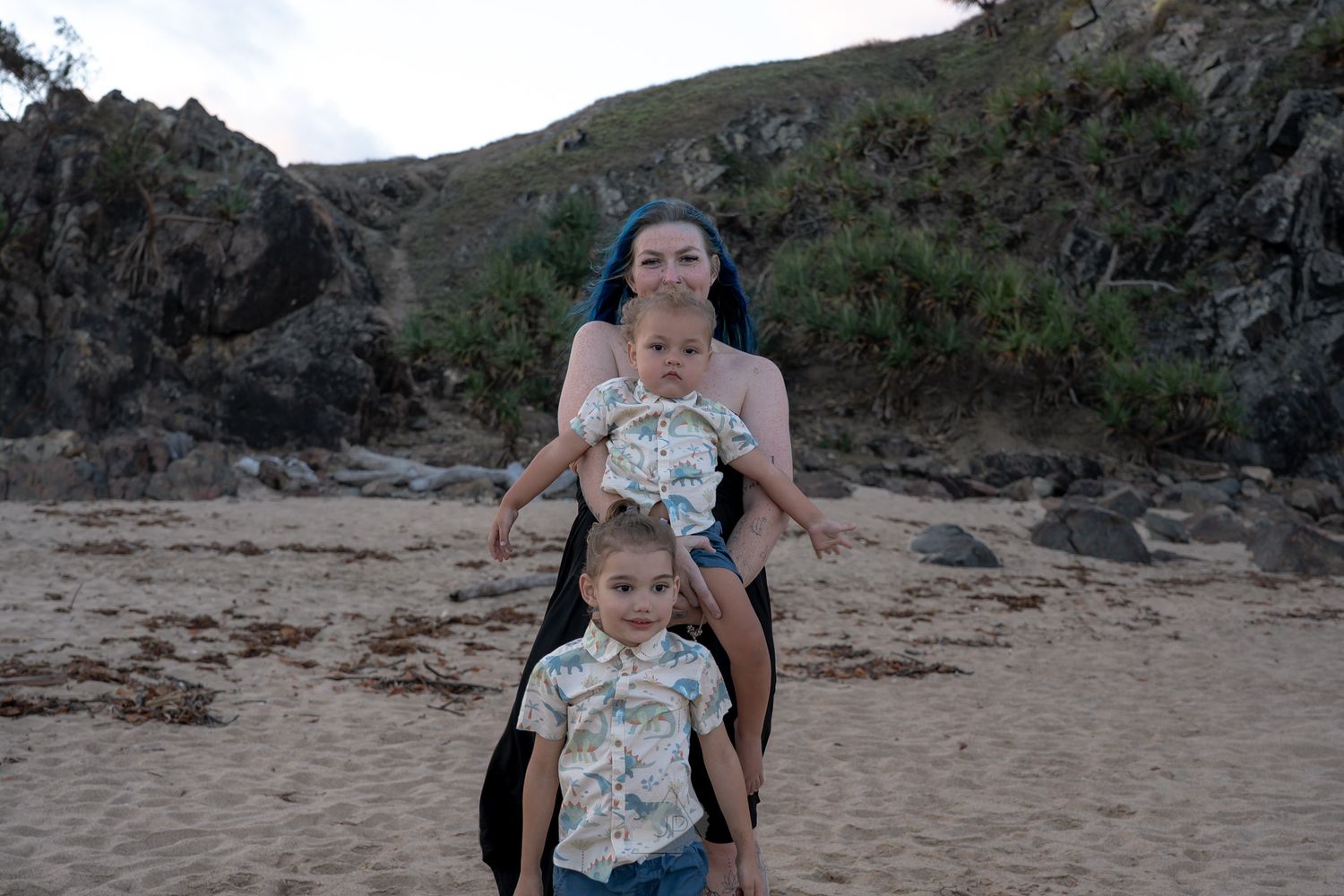 A person and child enjoy a sunny day at a rocky beach with cliffs in the background.