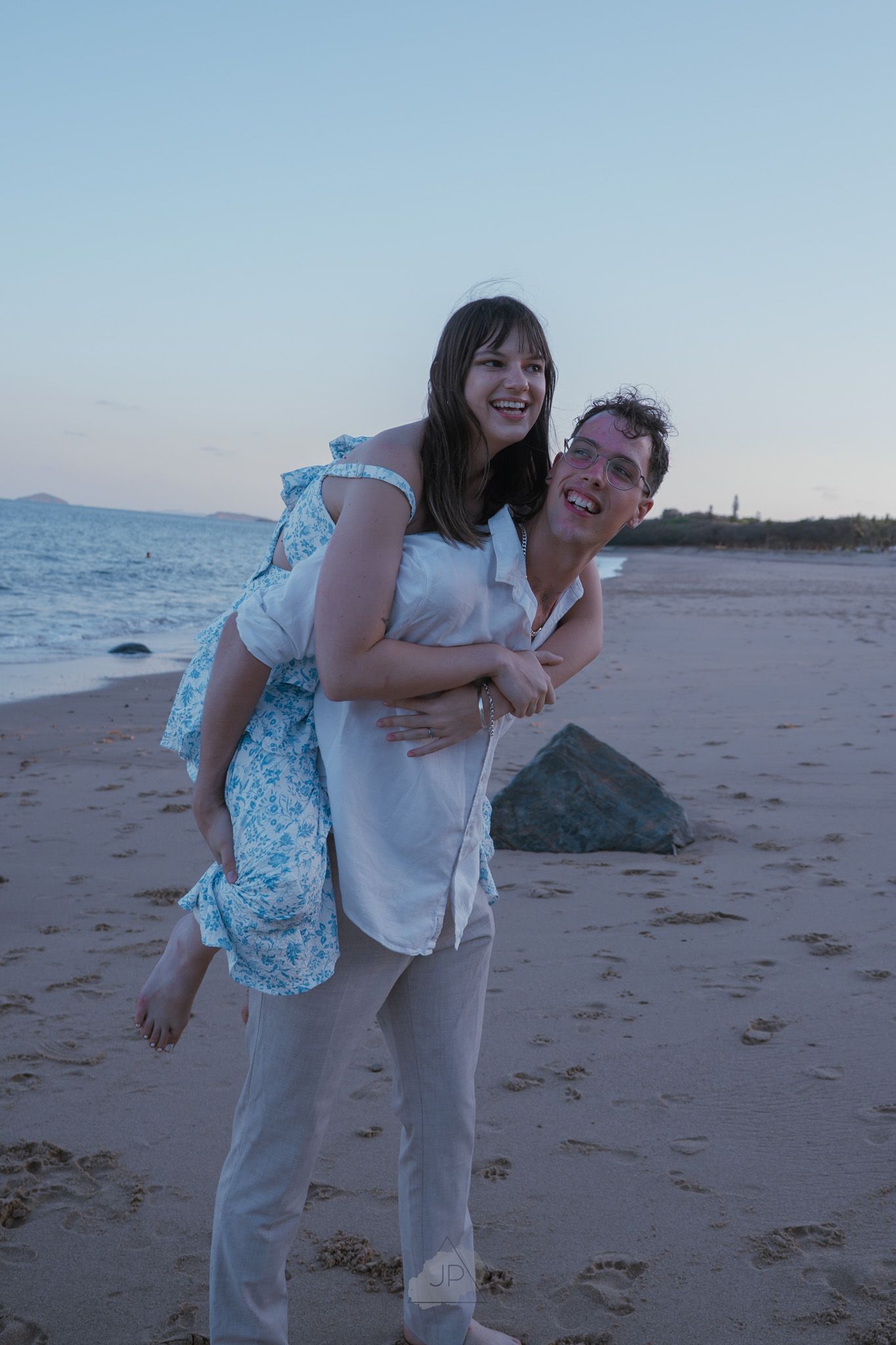 Two people share a playful moment together while walking on a sandy beach at sunset.